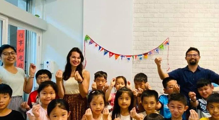 一群兒童和成人舉著手，在教室裡與橫幅合照。