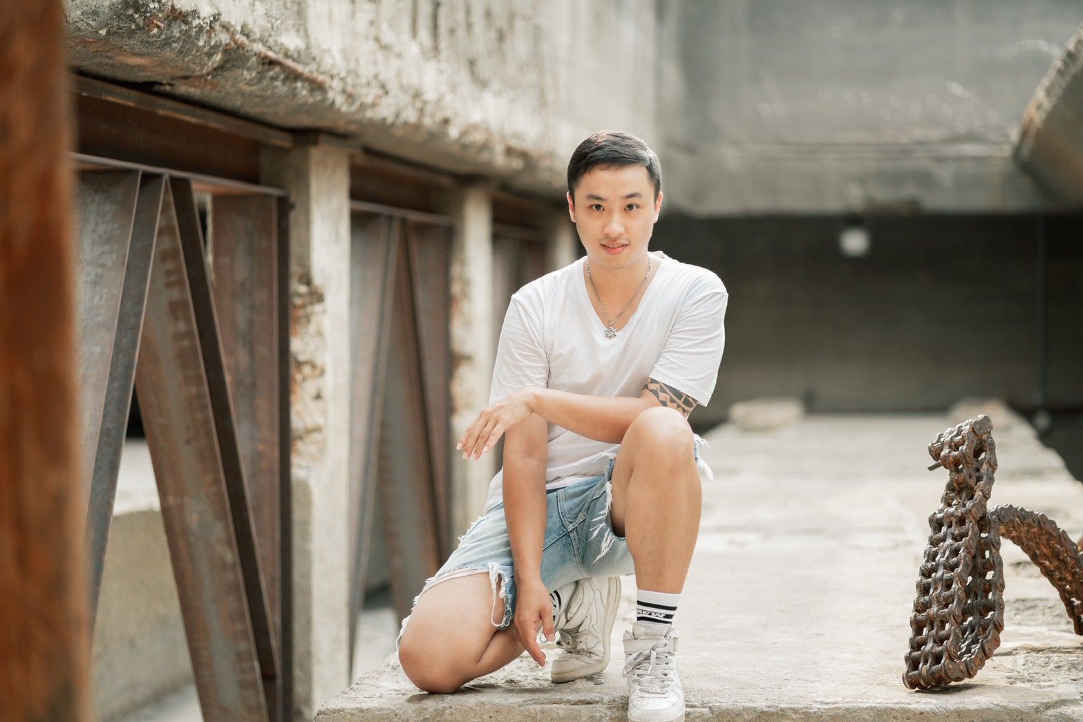 一名身穿白色T恤和牛仔短褲的男子蹲在混凝土結構下生鏽的金屬附近。