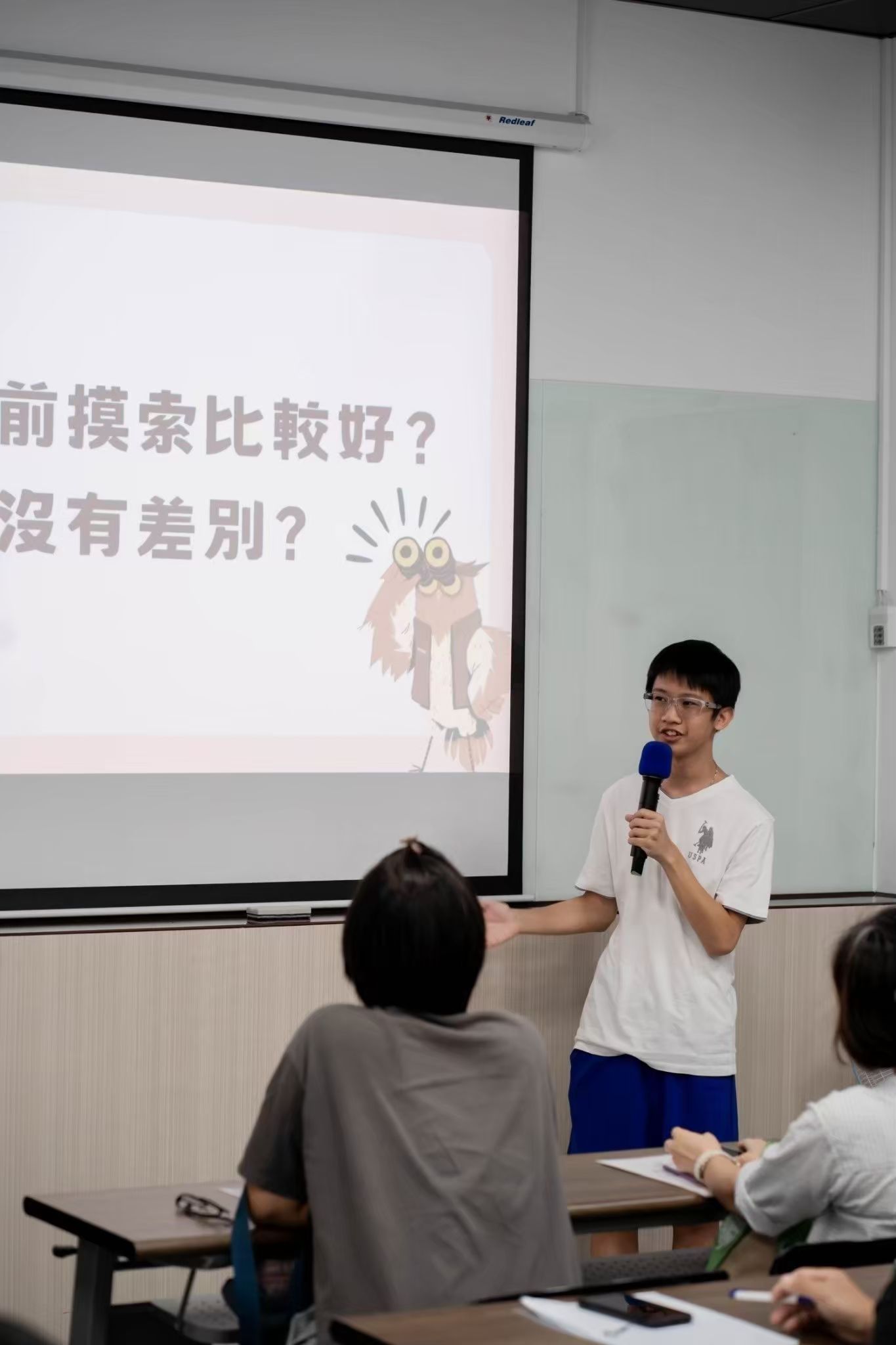 一位年輕男子在教室裡用麥克風演講。