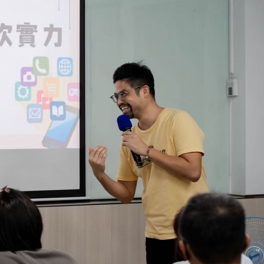 一位戴眼鏡、手持麥克風的男士面帶微笑地進行演講。螢幕上顯示著應用程式圖示。