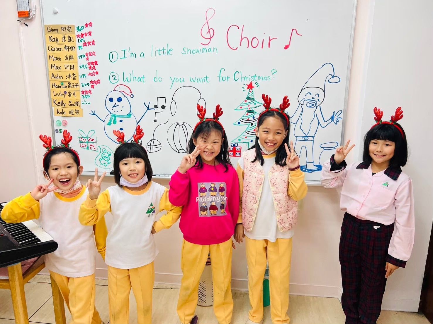五個戴著聖誕頭飾的孩子在唱詩班公告板前擺姿勢,比出和平手勢。
