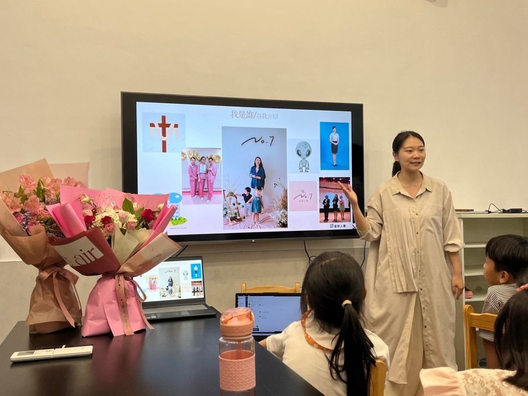 一位女士在教室裡做演講,教室螢幕播放圖片。前景是鮮花和兒童。