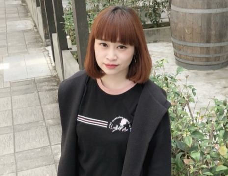 一名棕色短髮女子,身穿黑色襯衫和外套,站在戶外磚砌小路上。