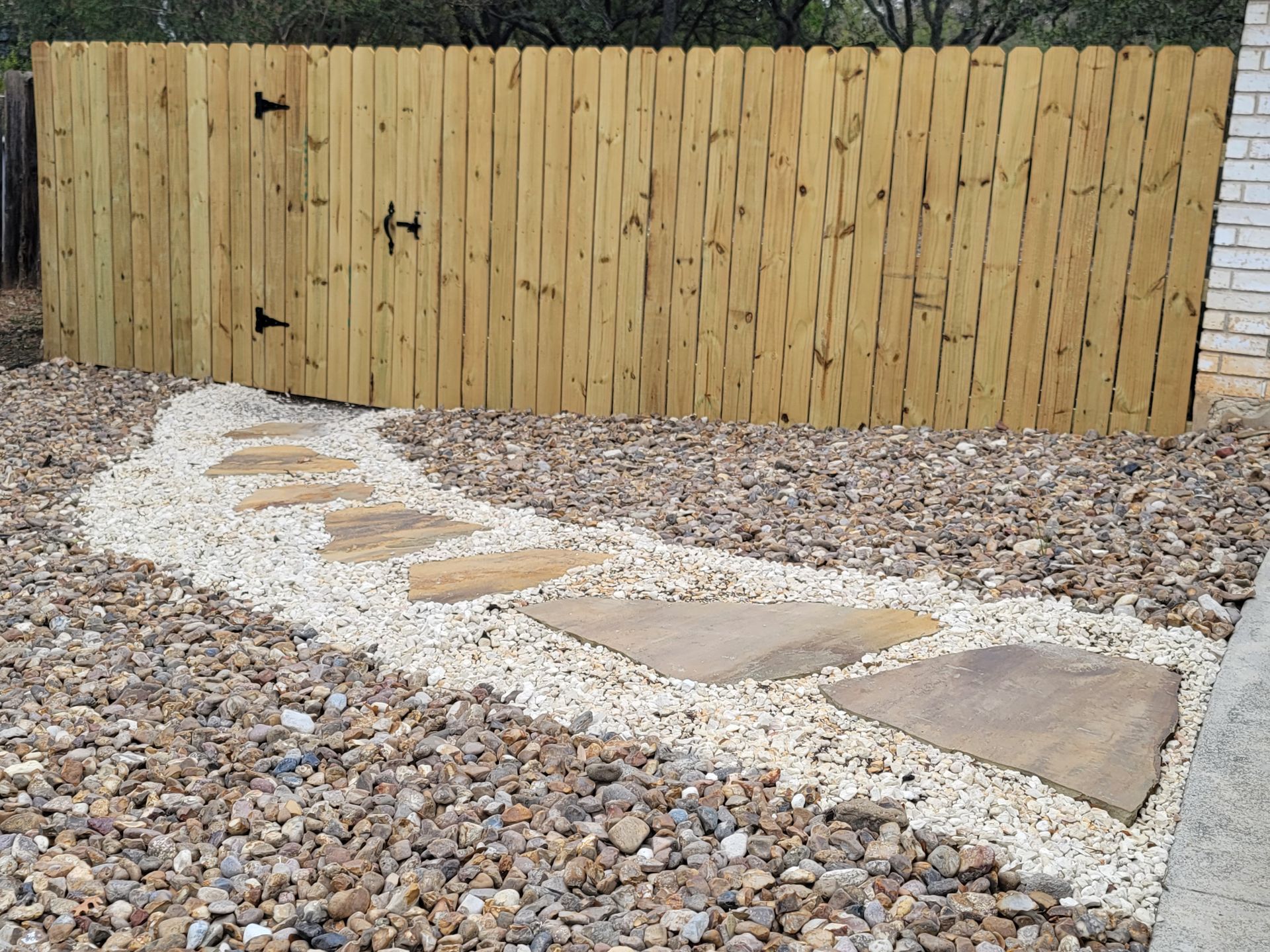 A wooden fence surrounds a gravel path in a backyard .