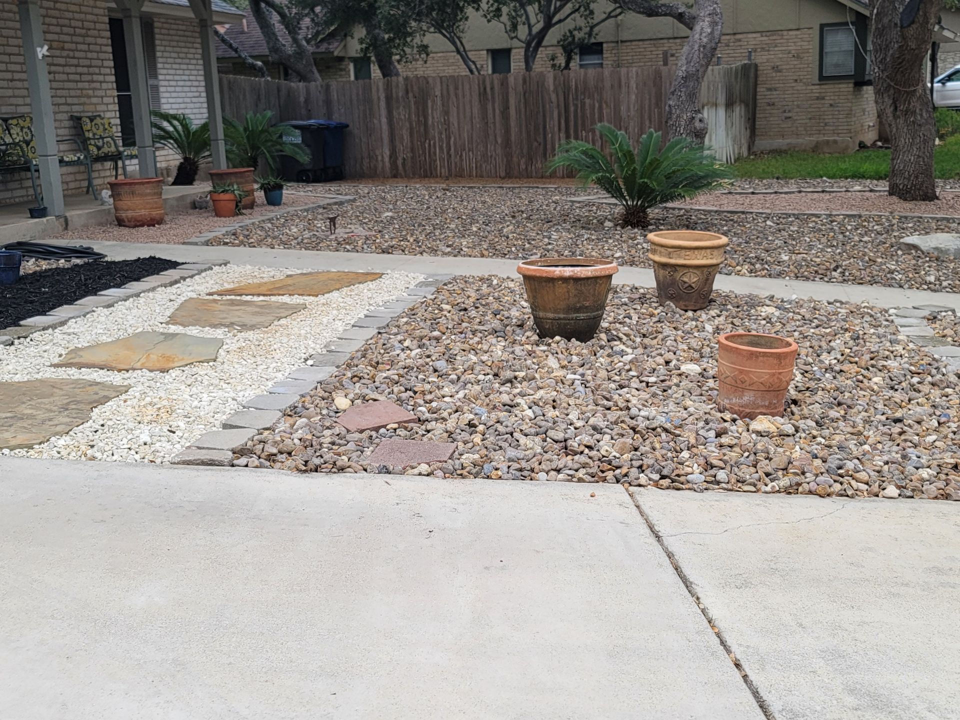 A concrete driveway with potted plants and a fence in the background