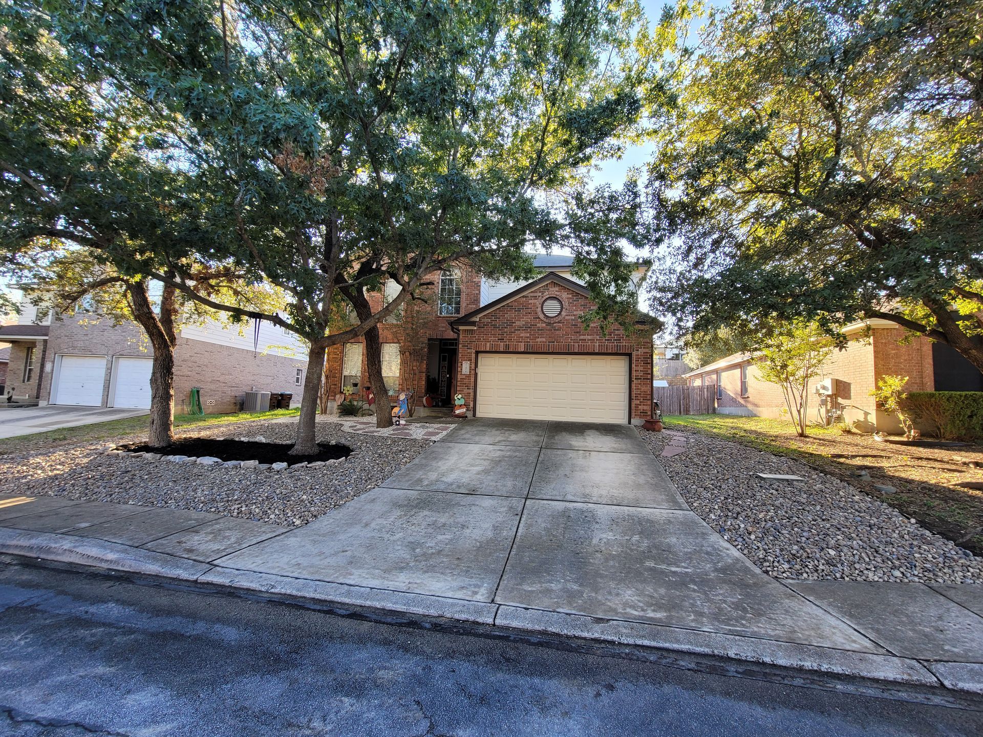 A brick house with a driveway and trees in front of it .
