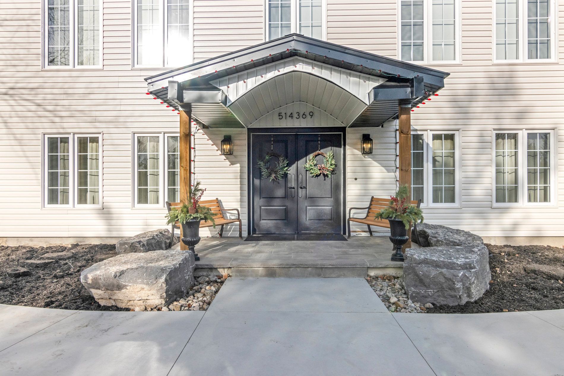 Entrance to a white building with black double doors, a canopy, benches, and large rocks.