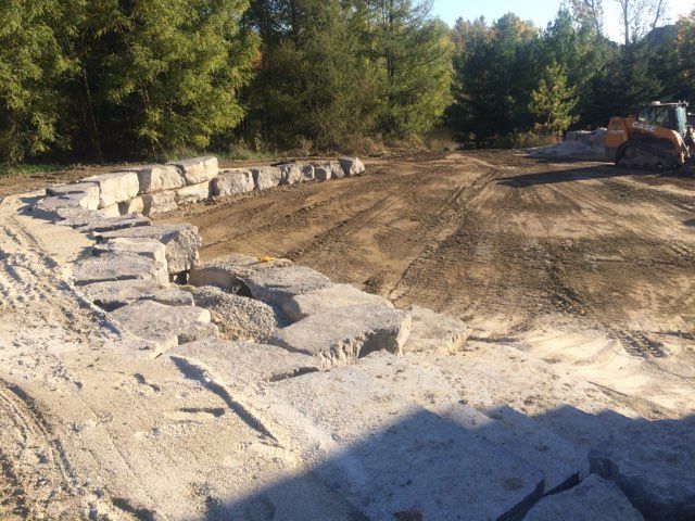 A bulldozer is driving down a dirt road next to a pile of rocks.