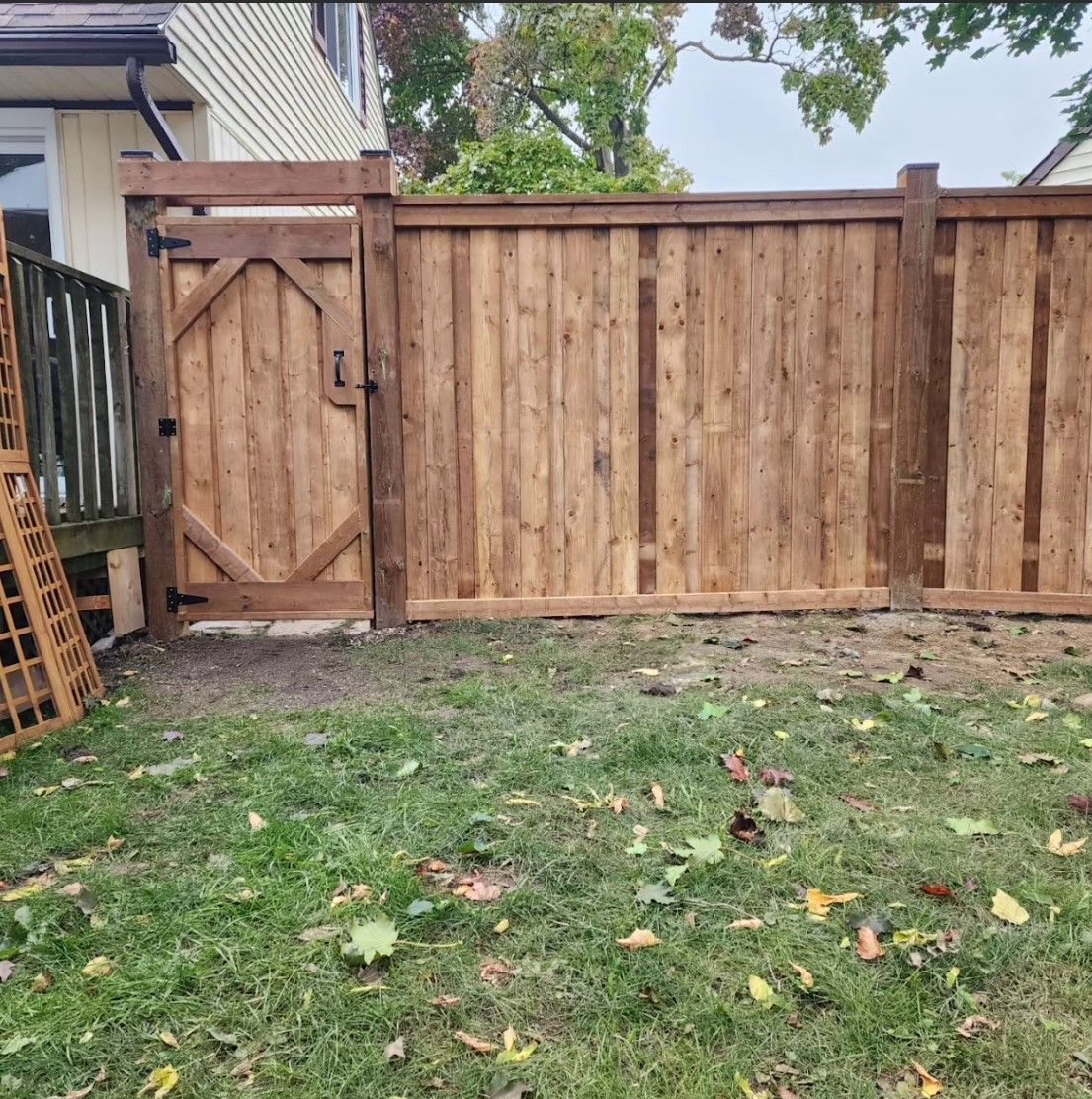 Wooden fence with gate in backyard; green grass and fallen leaves.
