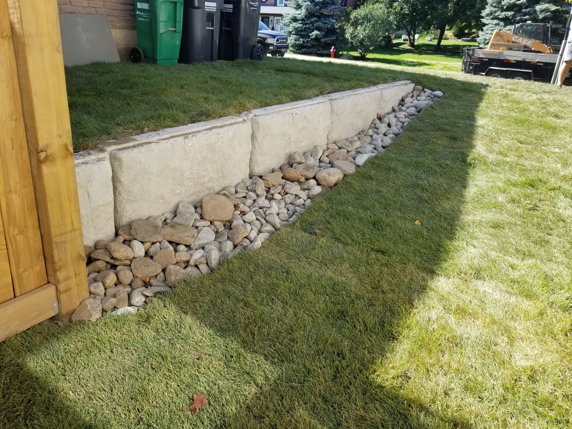 Concrete retaining wall with rocks and grass in a yard.