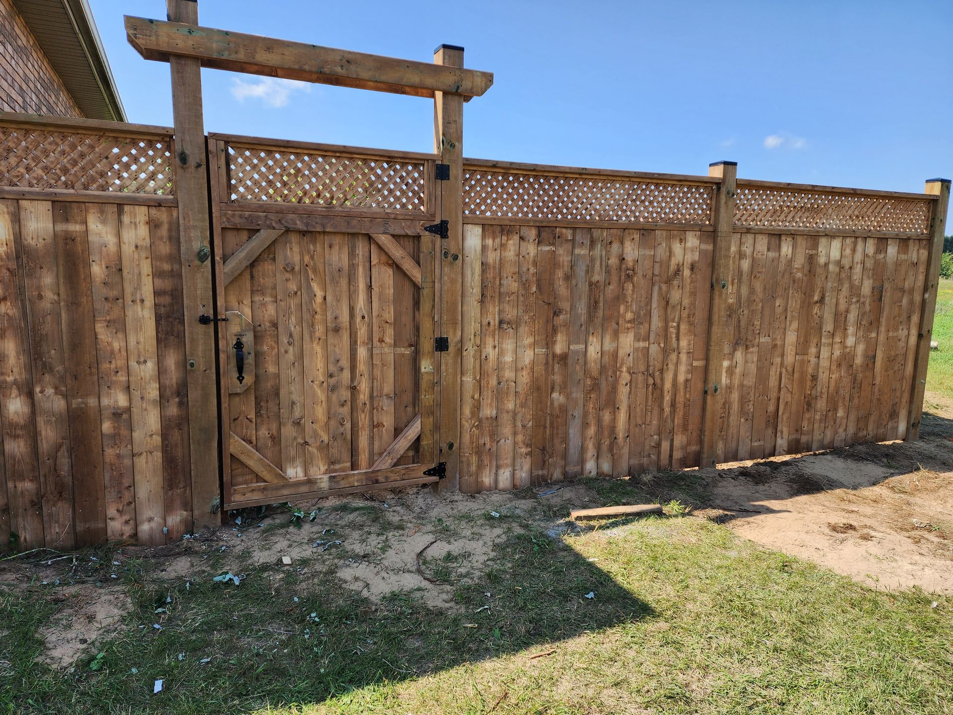 Wooden fence with gate, topped with lattice, in a sunny yard.