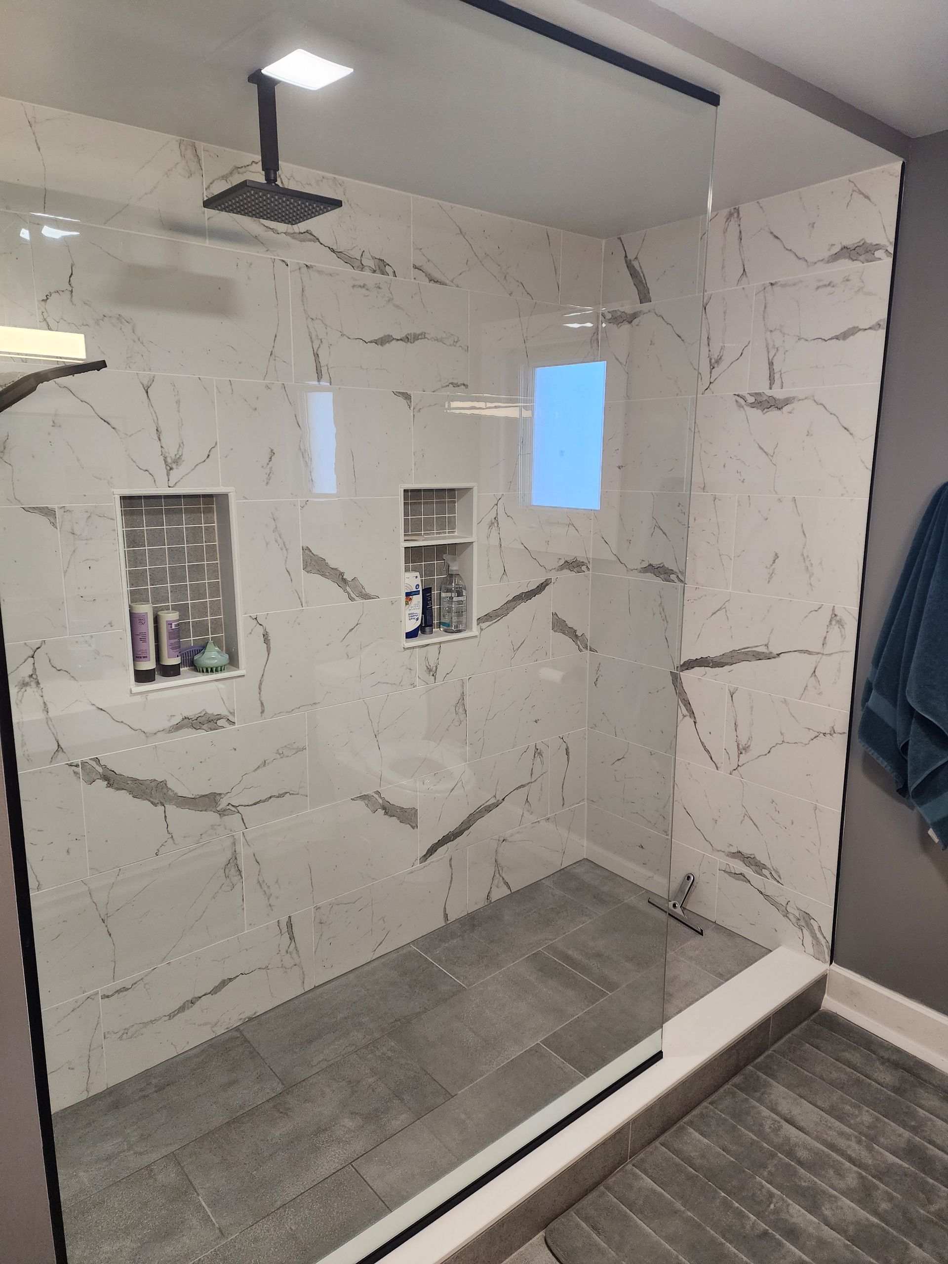Modern bathroom with marble-look tile shower, glass door, recessed shelves, and gray floor.