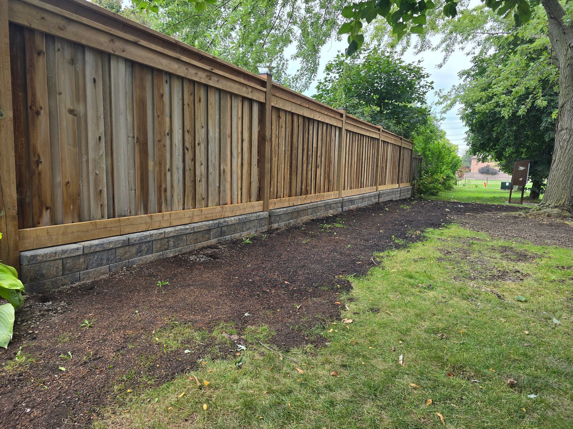 Wooden fence with a stone base, bordering a garden bed and lawn.