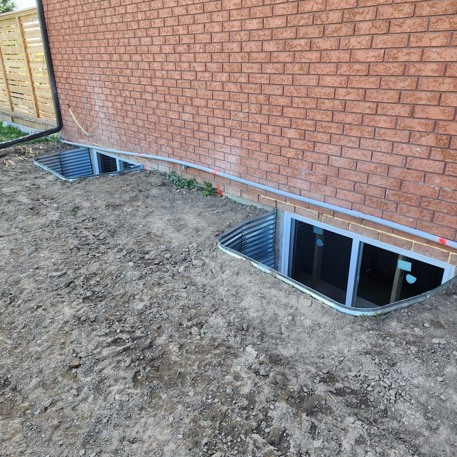 Exterior view of a brick house with window wells. Bare dirt surrounds the foundation.
