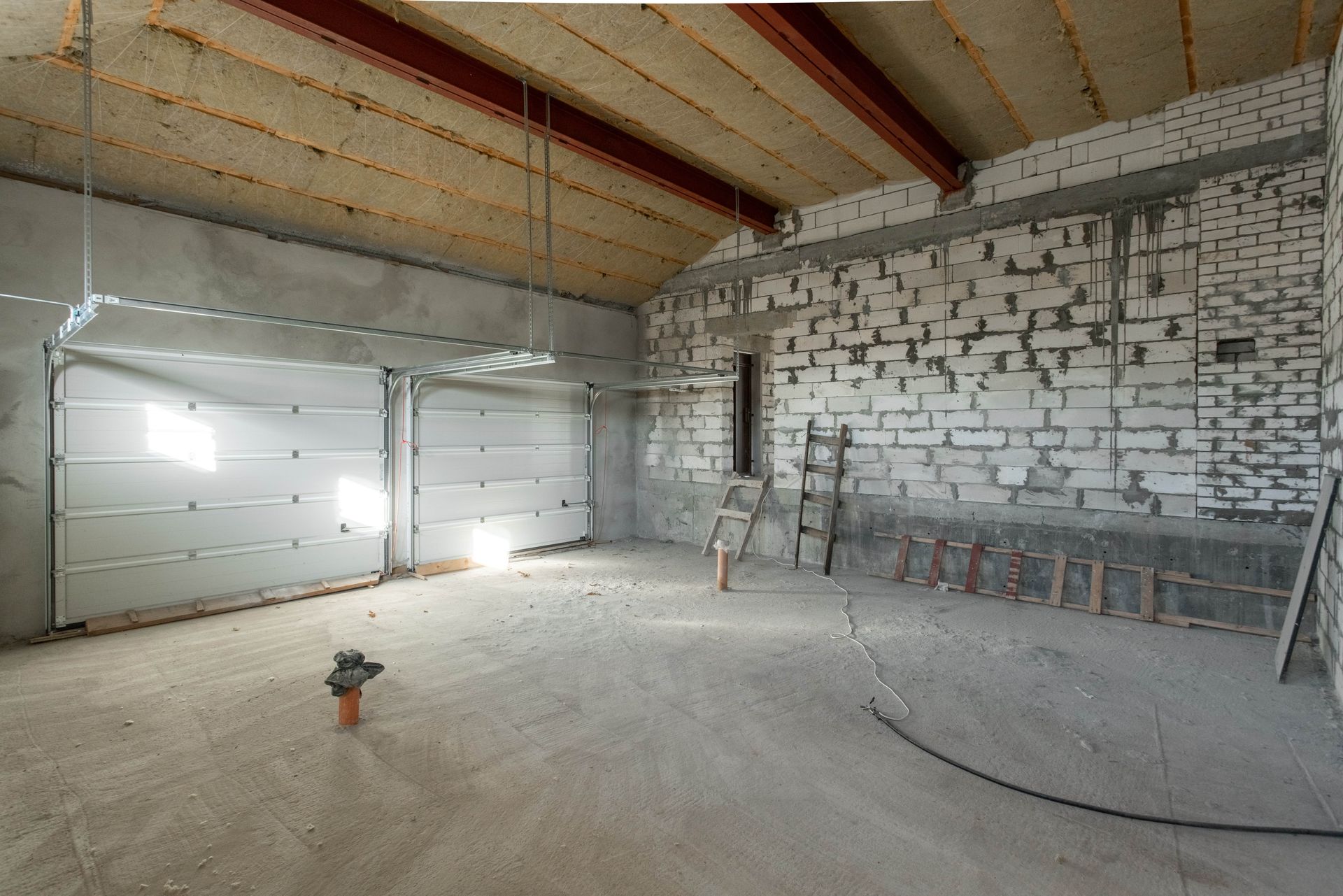 Interior of a partially constructed garage with unfinished walls, concrete floor, and two garage doors.