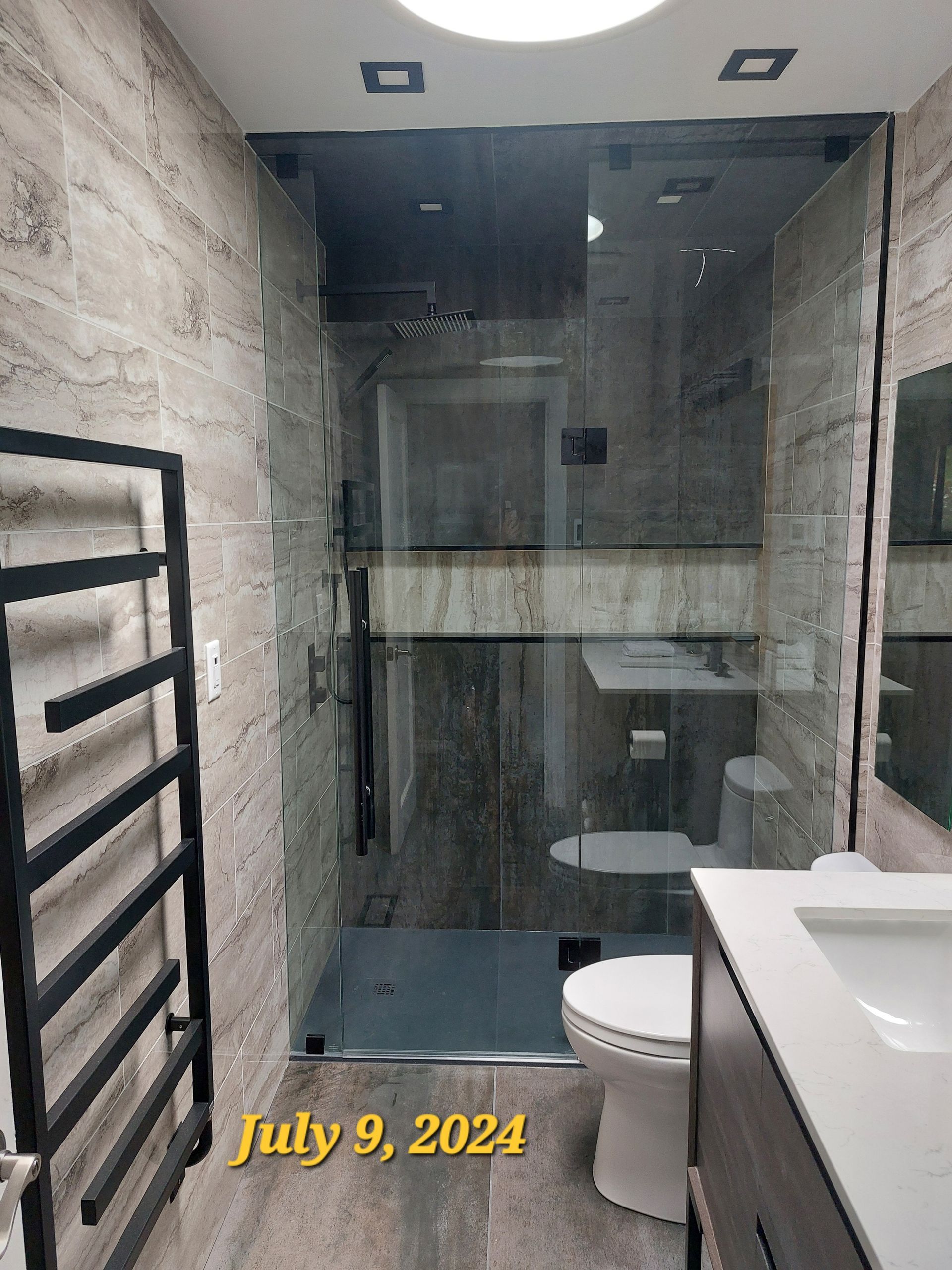 Modern bathroom with glass shower, toilet, vanity, and heated towel rack. Gray and brown color scheme.