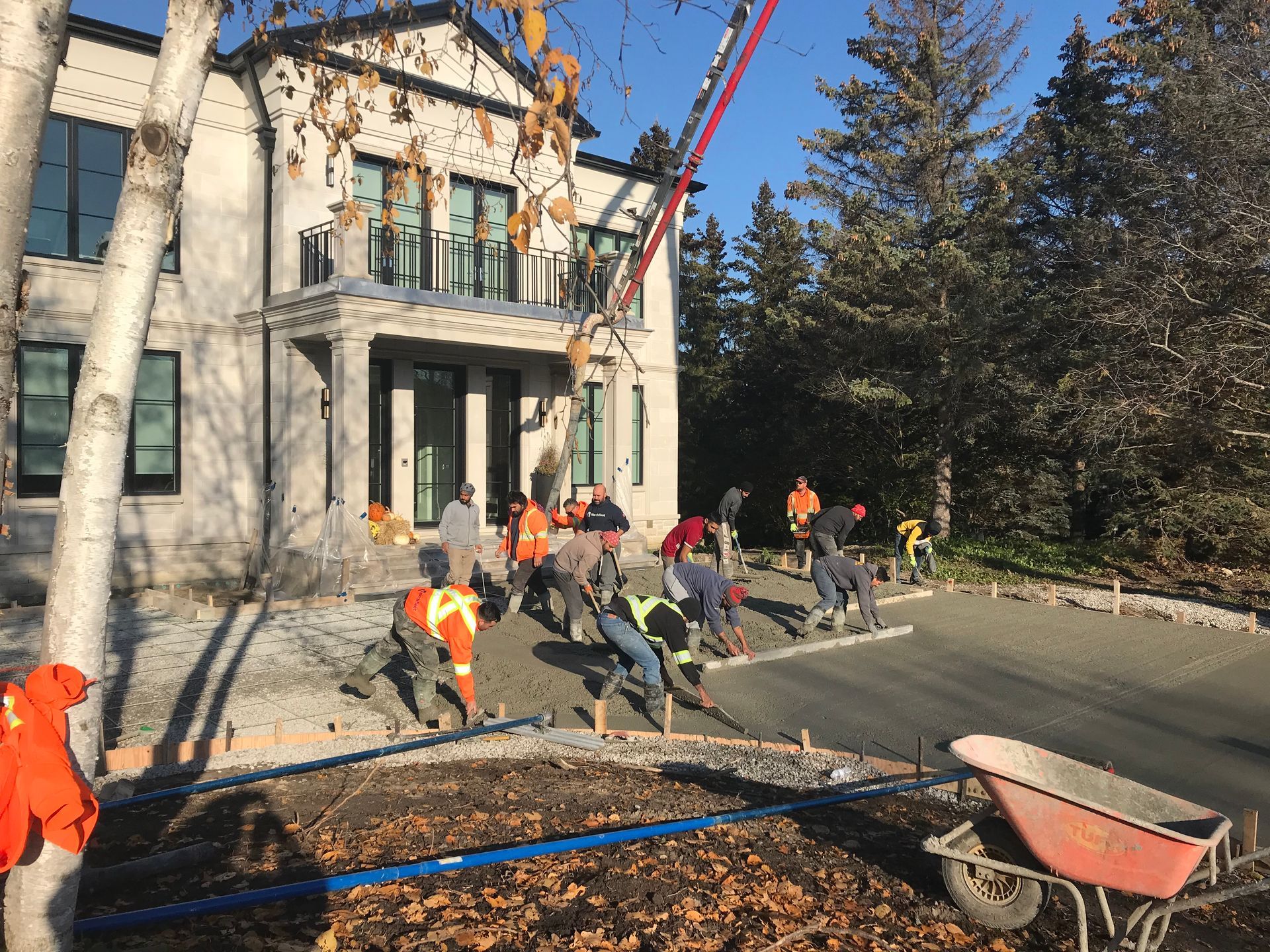 Construction workers pouring concrete driveway in front of a large house.