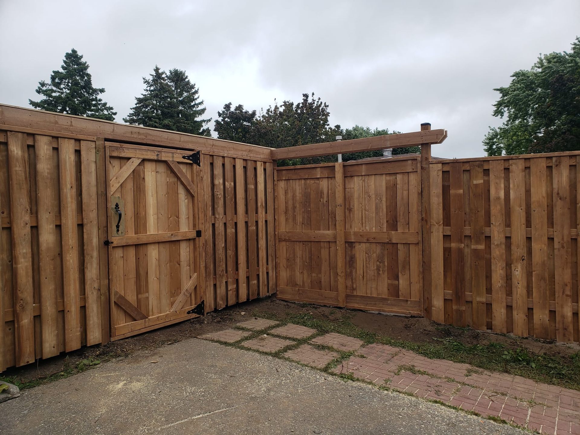 Wooden fence with two gates, one arched. Brown wood against a cloudy sky.