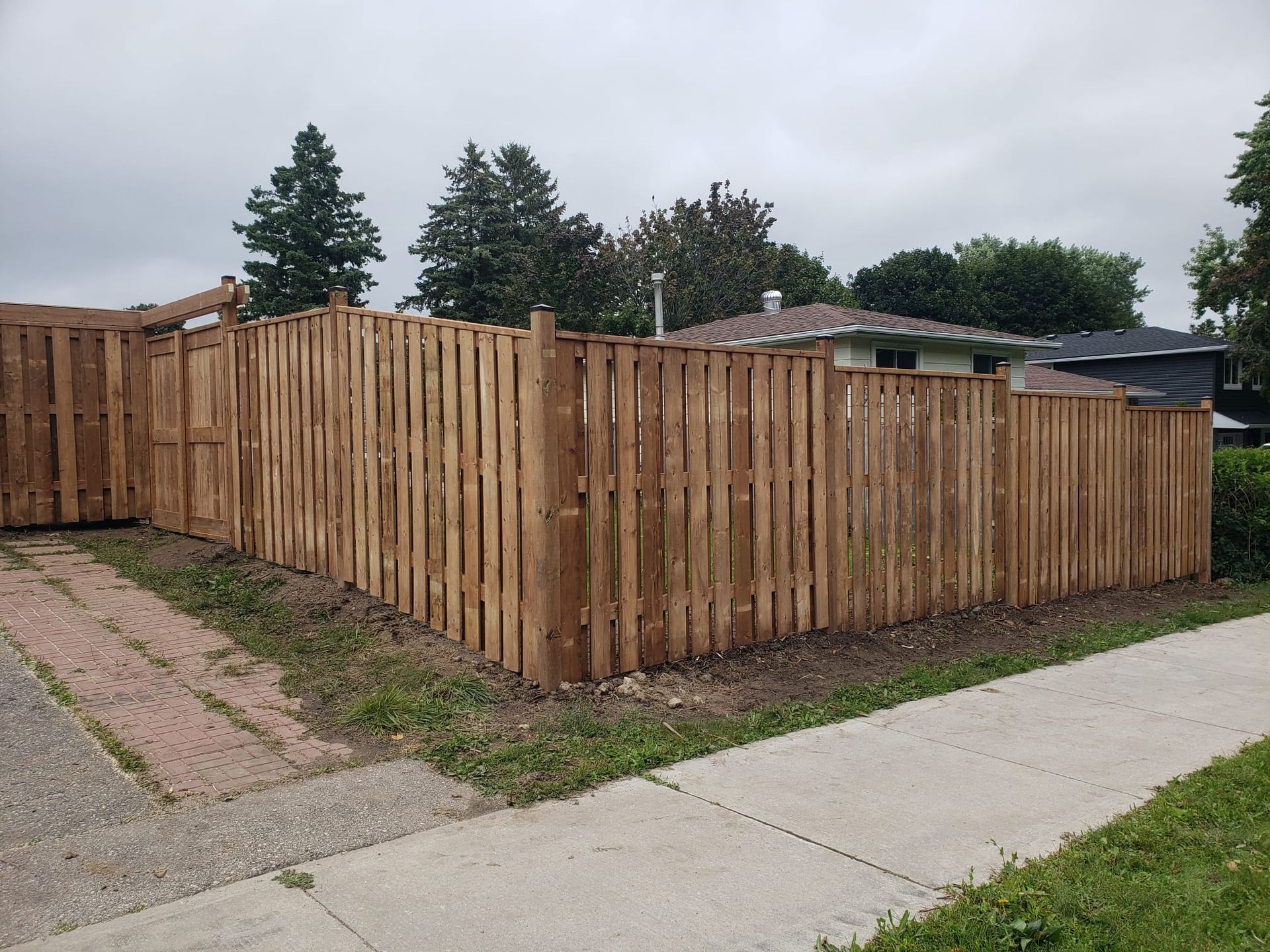Wooden privacy fence in a residential area, brown wood, sidewalk in foreground.