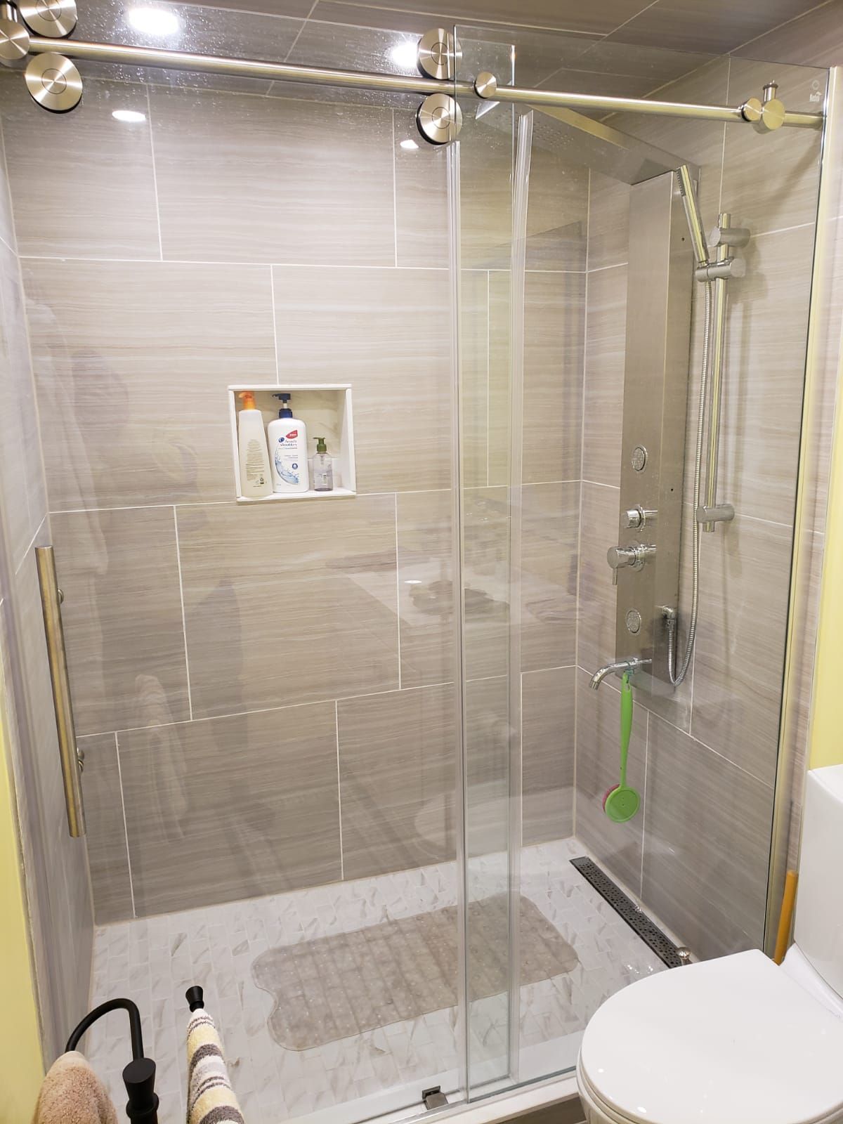 Modern shower with glass doors, gray tile, stainless steel fixtures, and a white toilet.