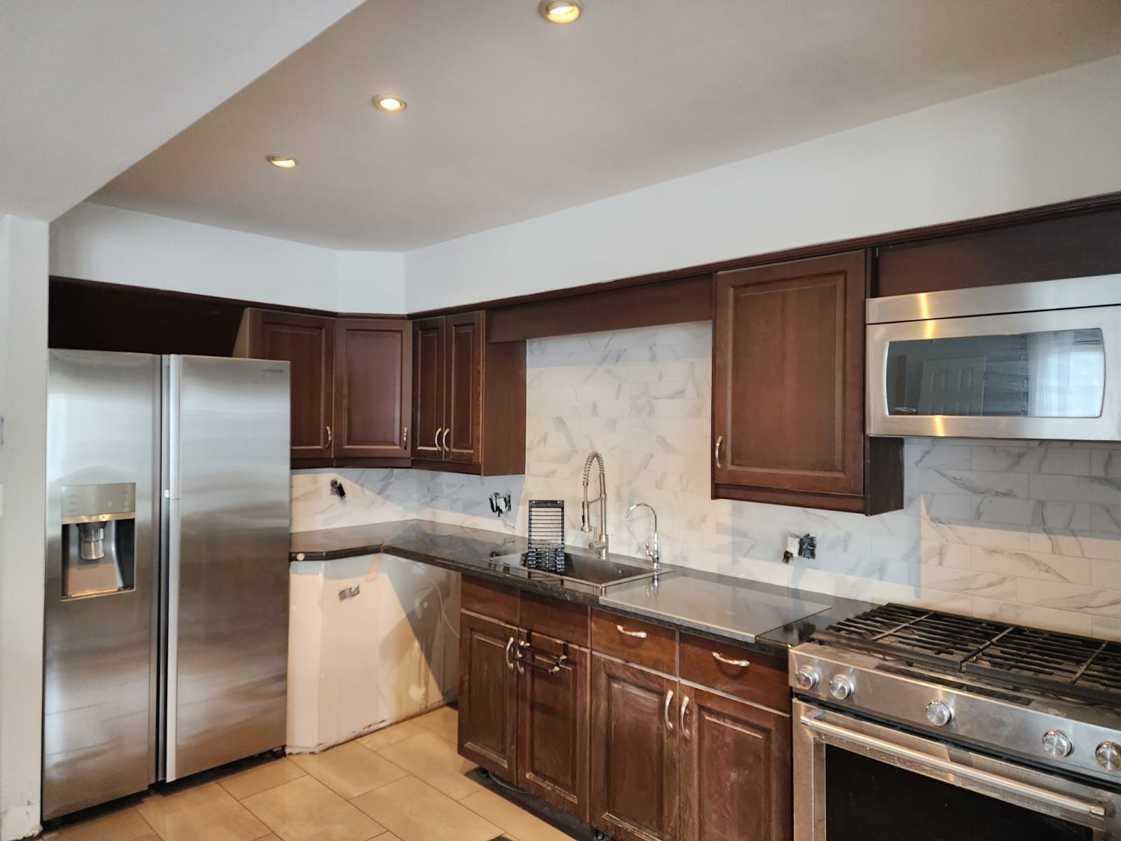 Kitchen with dark brown cabinets, stainless steel appliances, and marble backsplash.