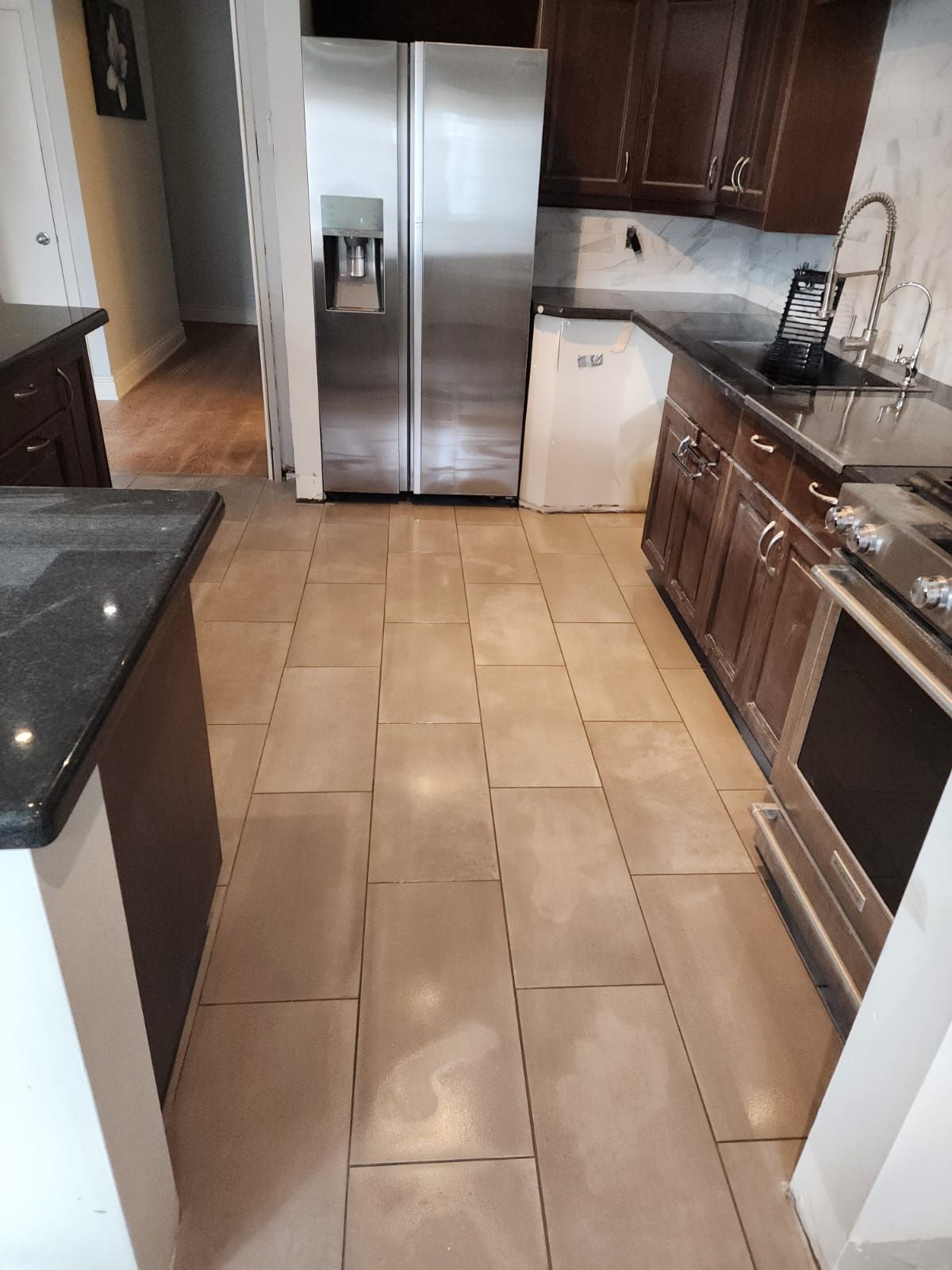 Kitchen with beige tile floor, stainless steel refrigerator, and dark cabinets.
