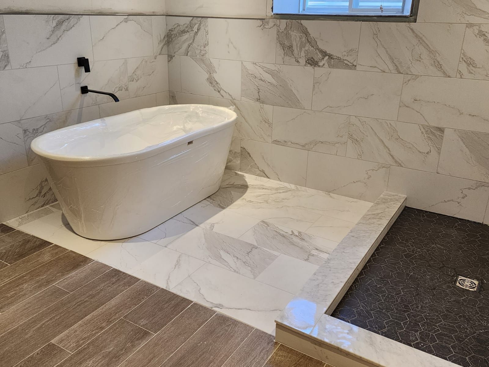 Modern bathroom with white freestanding tub, marble tile walls and floor, and a dark shower.