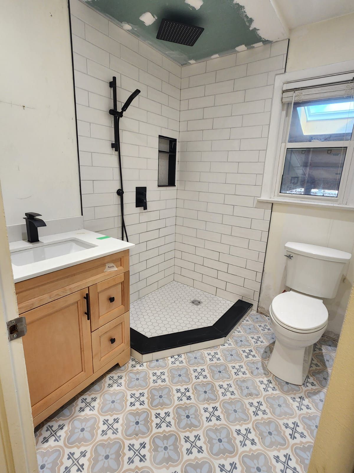 Bathroom renovation with white subway tile shower, black fixtures, and patterned floor.