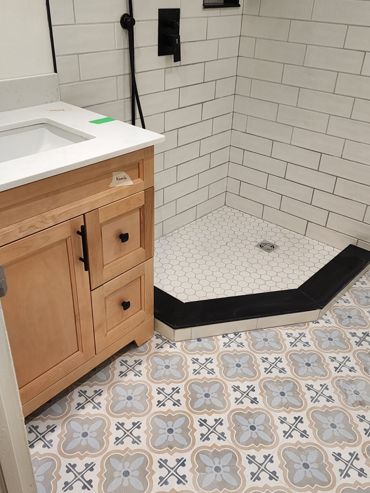 Bathroom with wooden vanity, tiled shower, and patterned floor tiles.