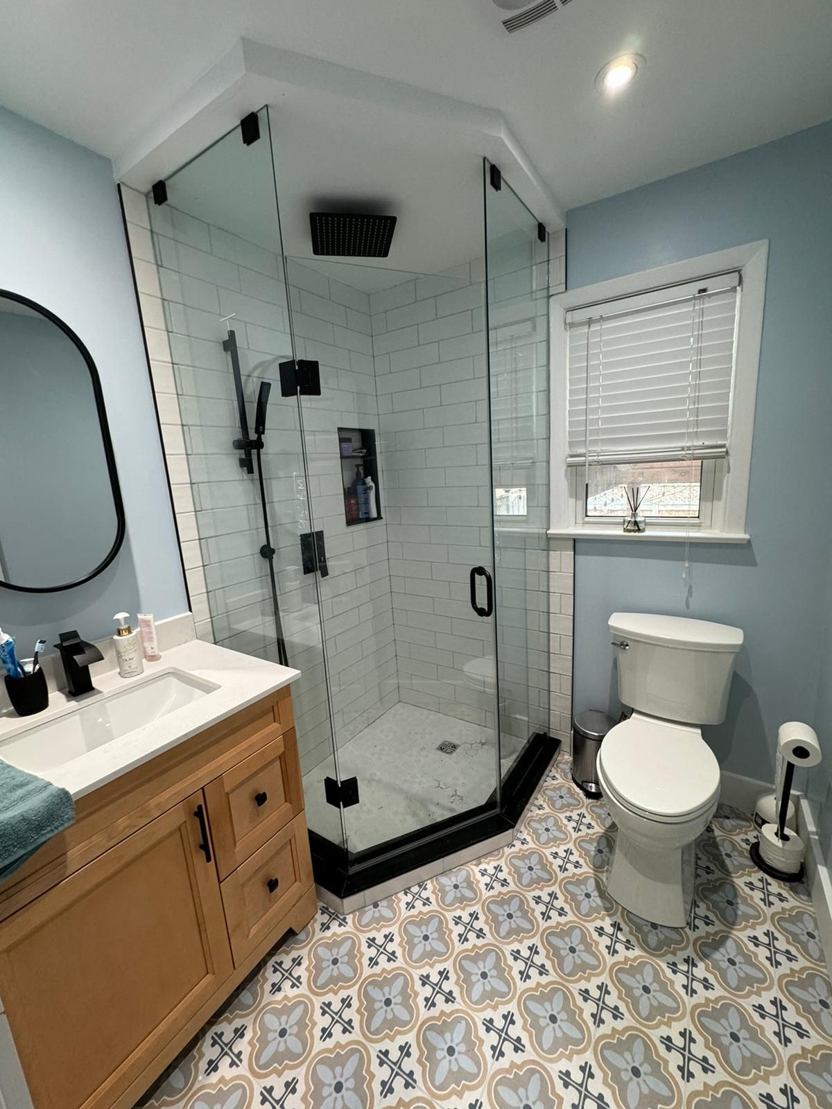 Bathroom with glass shower, light blue walls, wood vanity, and patterned tile floor.