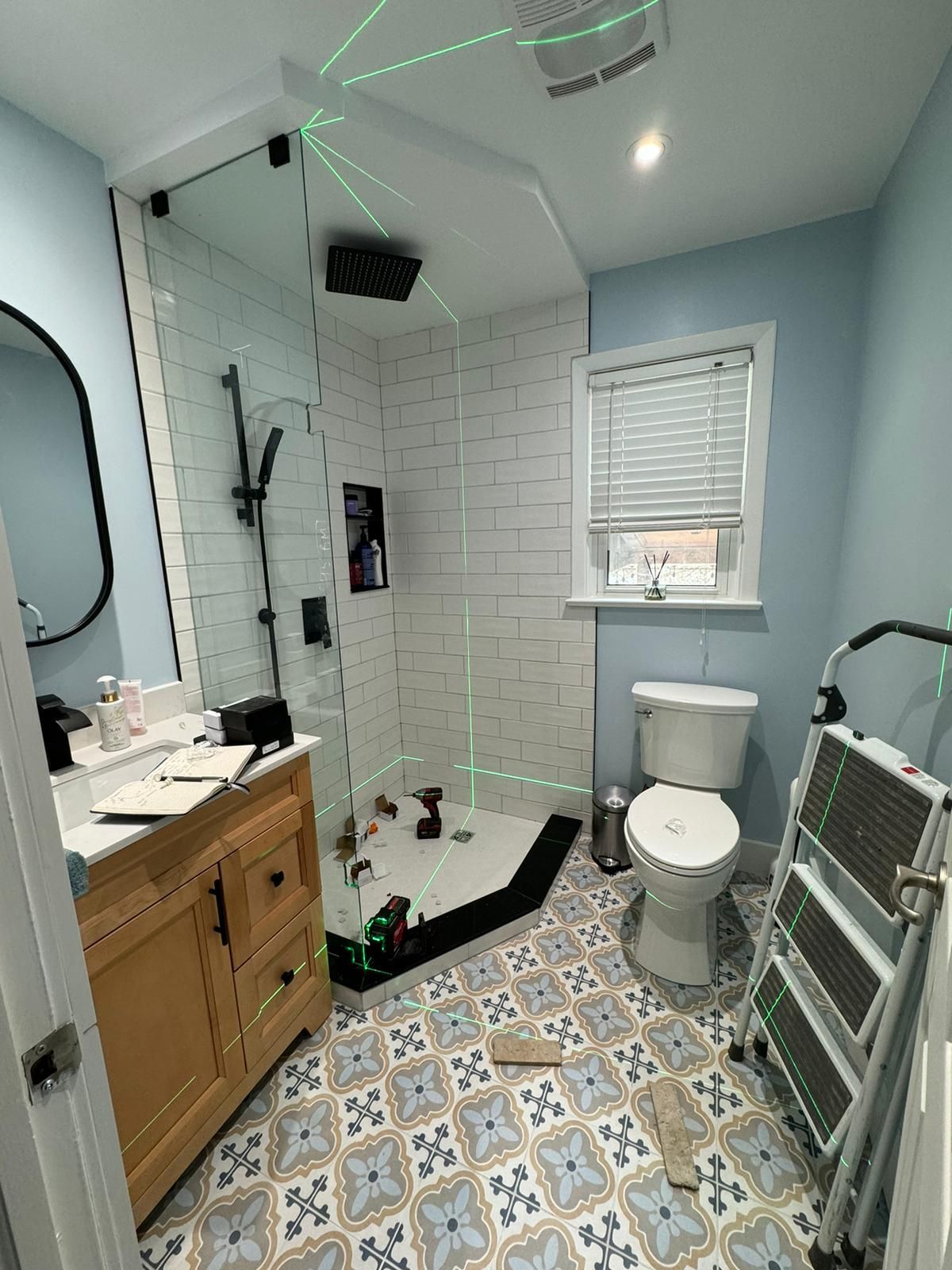 Bathroom renovation in progress with blue walls, patterned floor, shower, toilet, and tools.