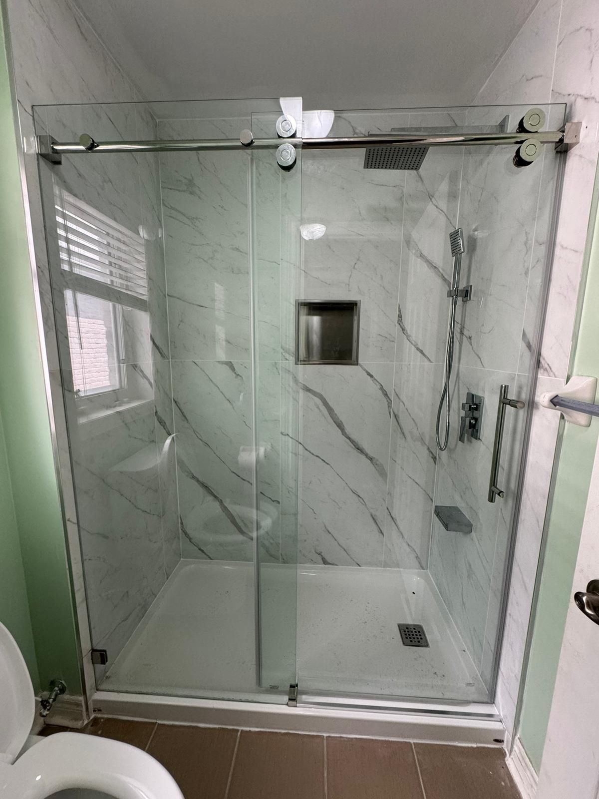 Modern glass shower enclosure in a bathroom with marble-patterned walls and a sliding door.