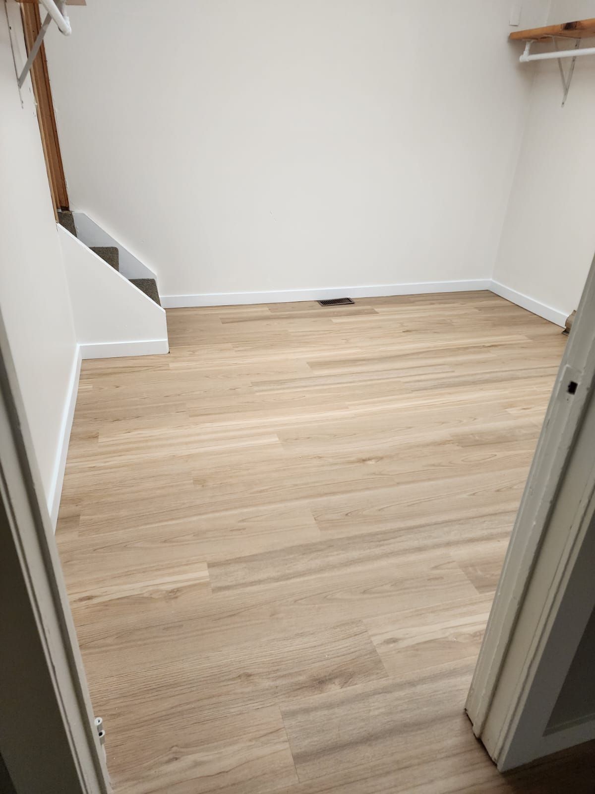 Empty room with light wood-look flooring and white walls. Small staircase to the left.