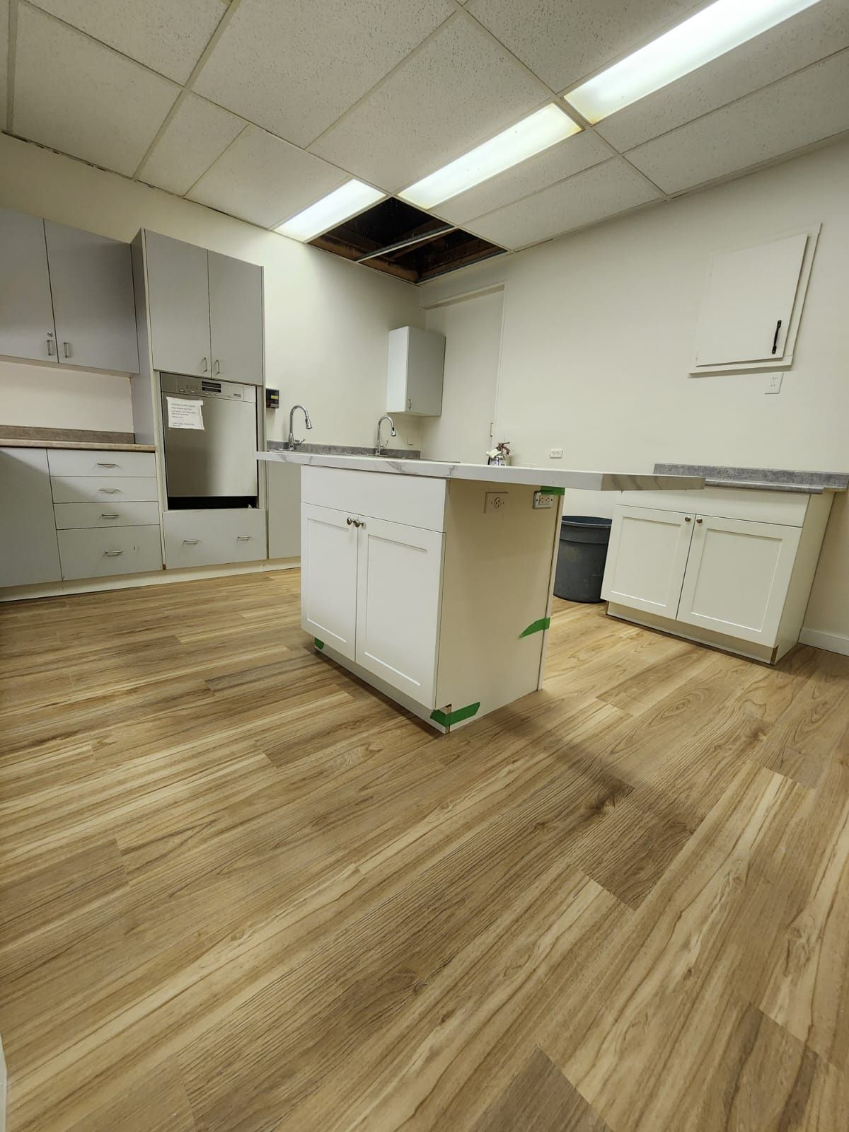 Kitchen with white cabinets, island, and wood-look flooring. Hole in ceiling.