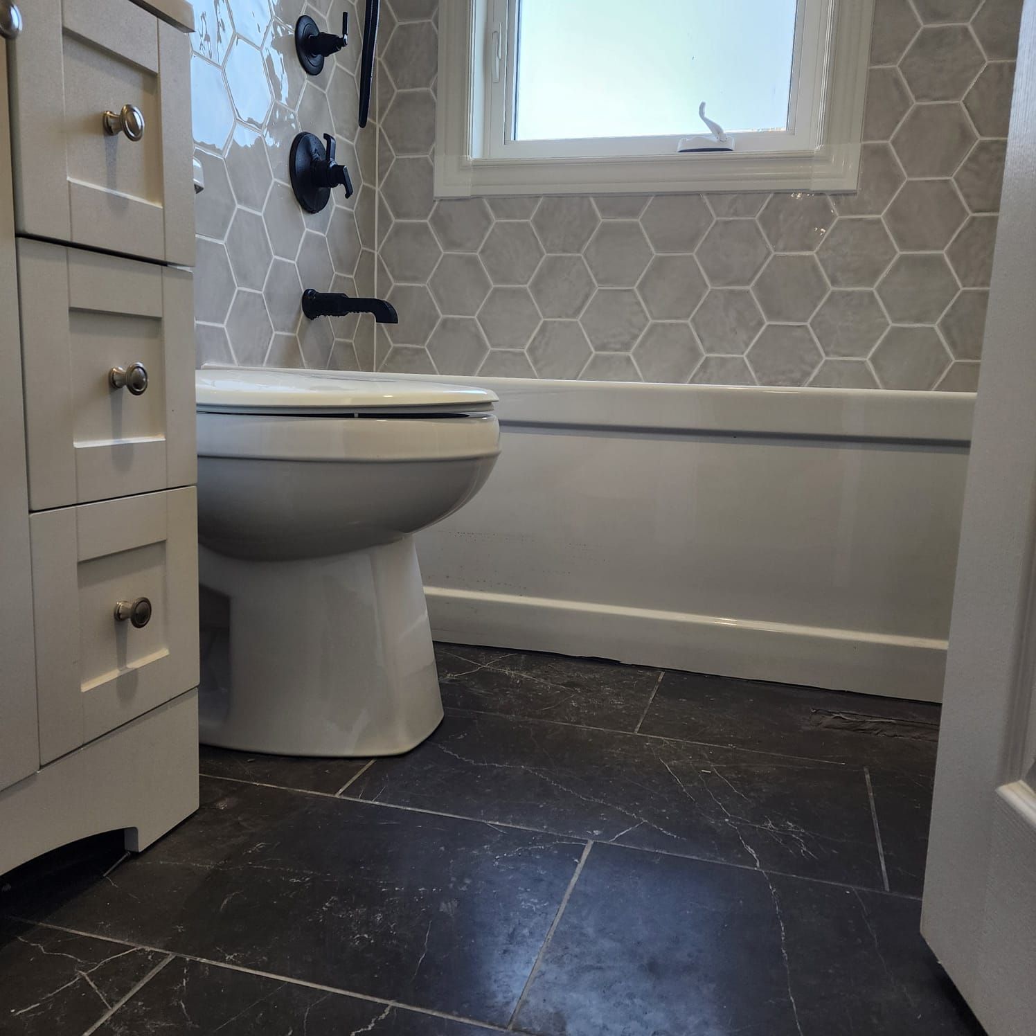 Bathroom with a white toilet, gray hexagon tile backsplash, and dark gray floor tiles.