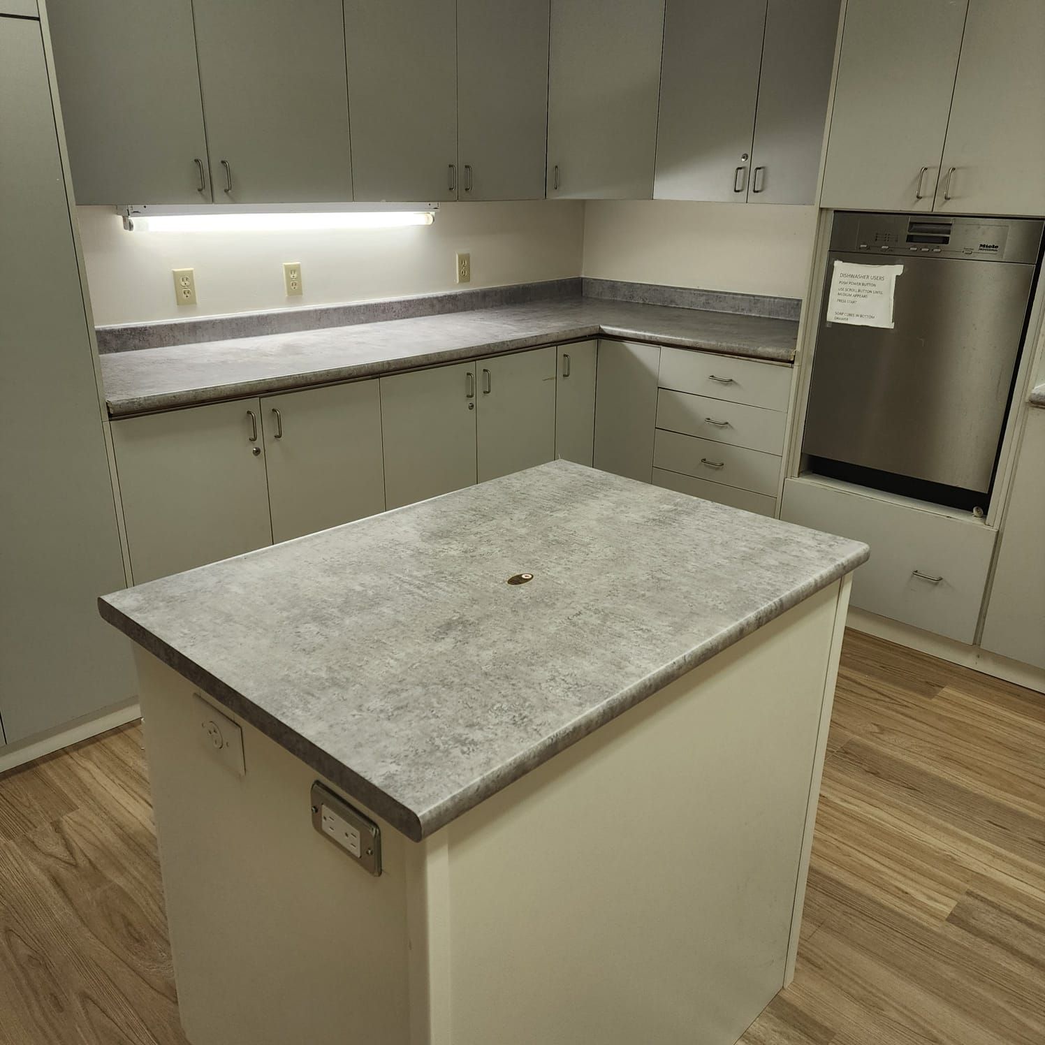 Kitchen with light cabinets, gray countertops, and an island. Stainless steel dishwasher.