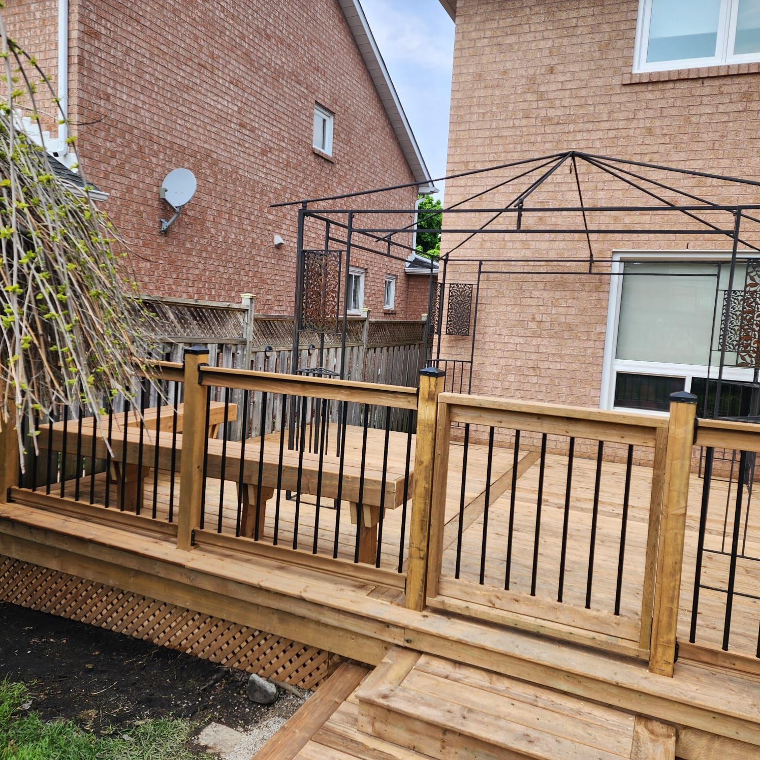 Wooden deck with black railings and gazebo, near brick buildings.