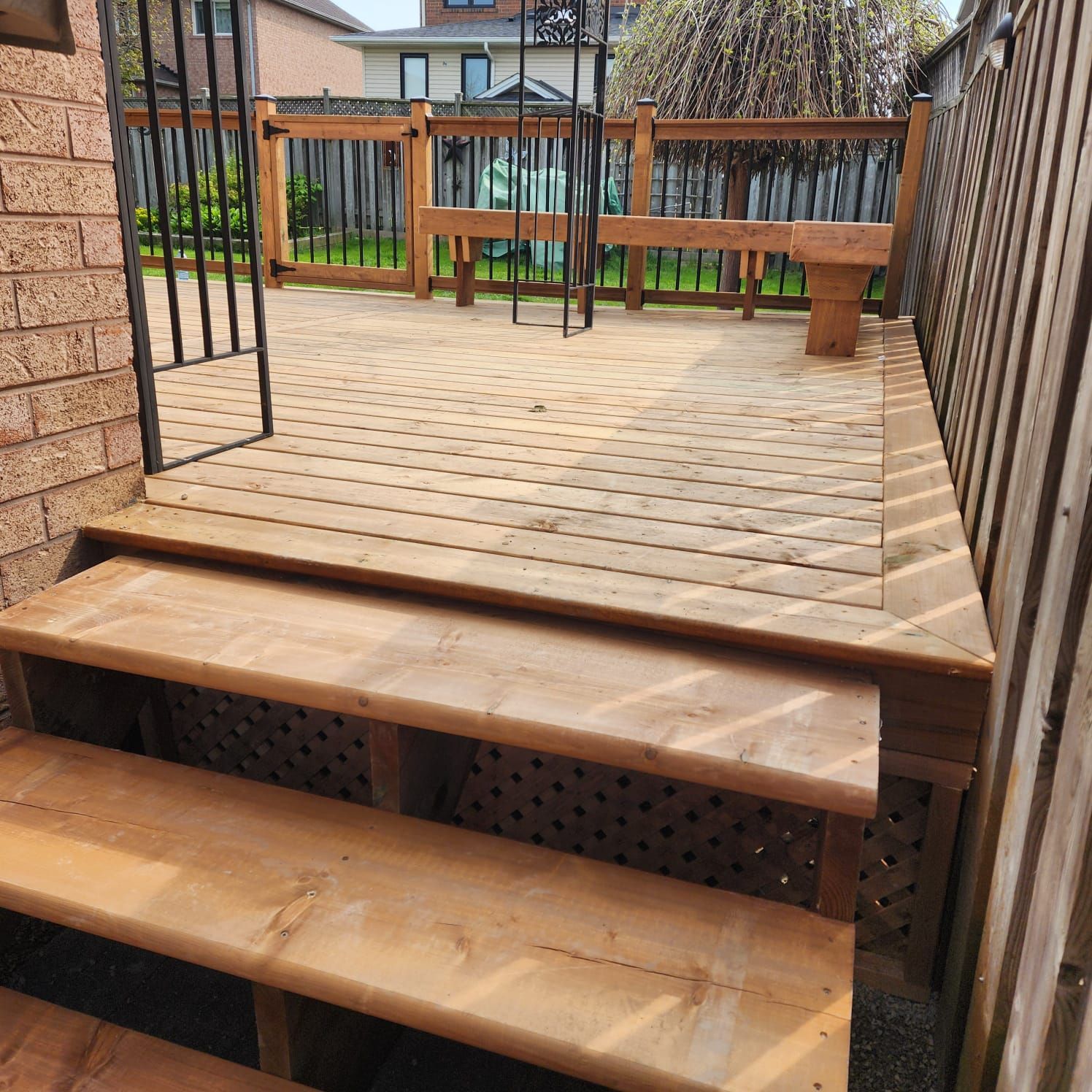 Wooden deck with steps, a gate, and bench in a backyard.