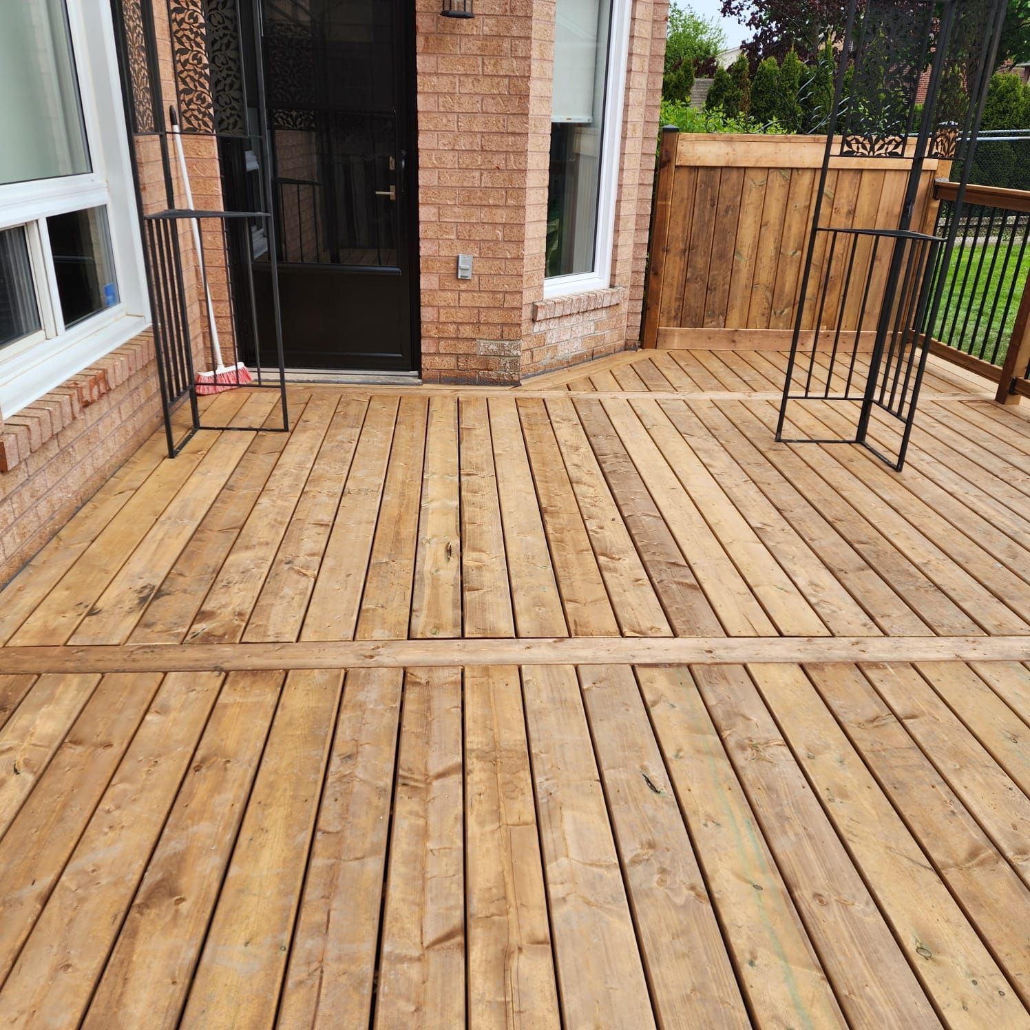 Wooden deck outside a brick building with a door, railings, and a window.