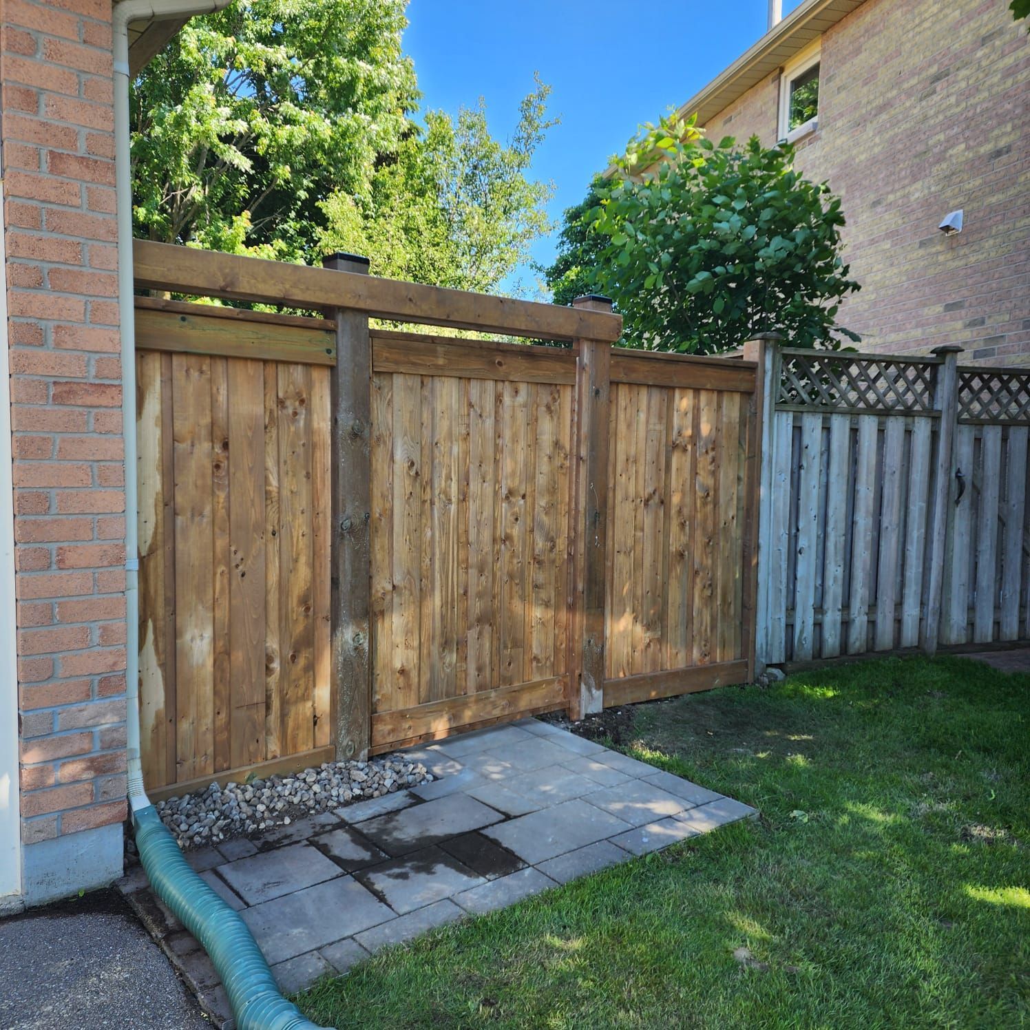 Wooden fence between a brick building and a grassy yard.