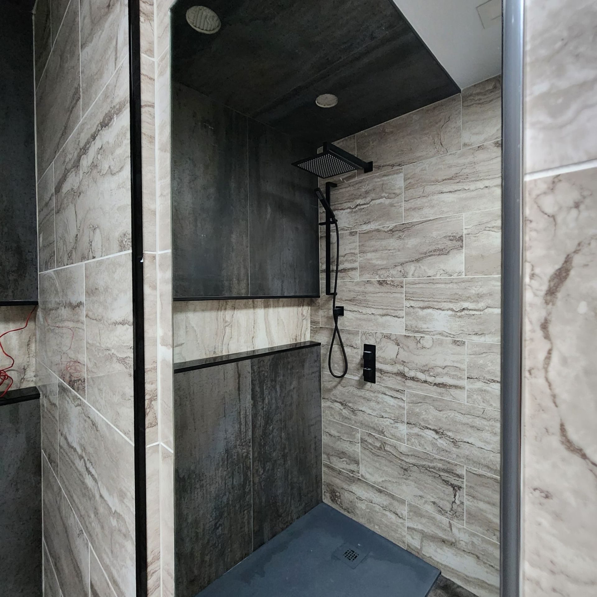 Shower with grey stone-like wall tiles, dark grey ceiling and shower head, and dark grey floor.