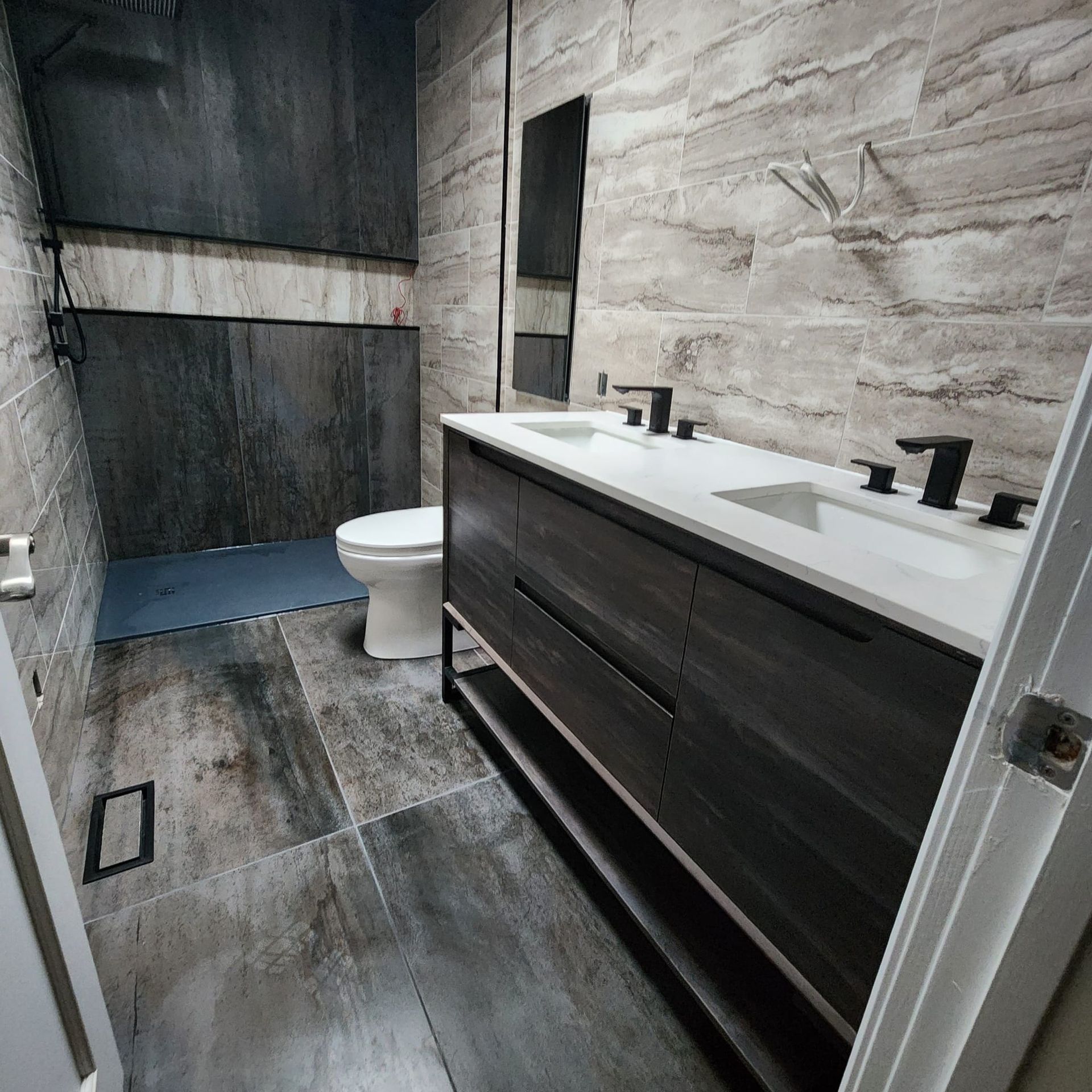 Modern bathroom with gray tile, a double sink vanity, toilet, and shower.