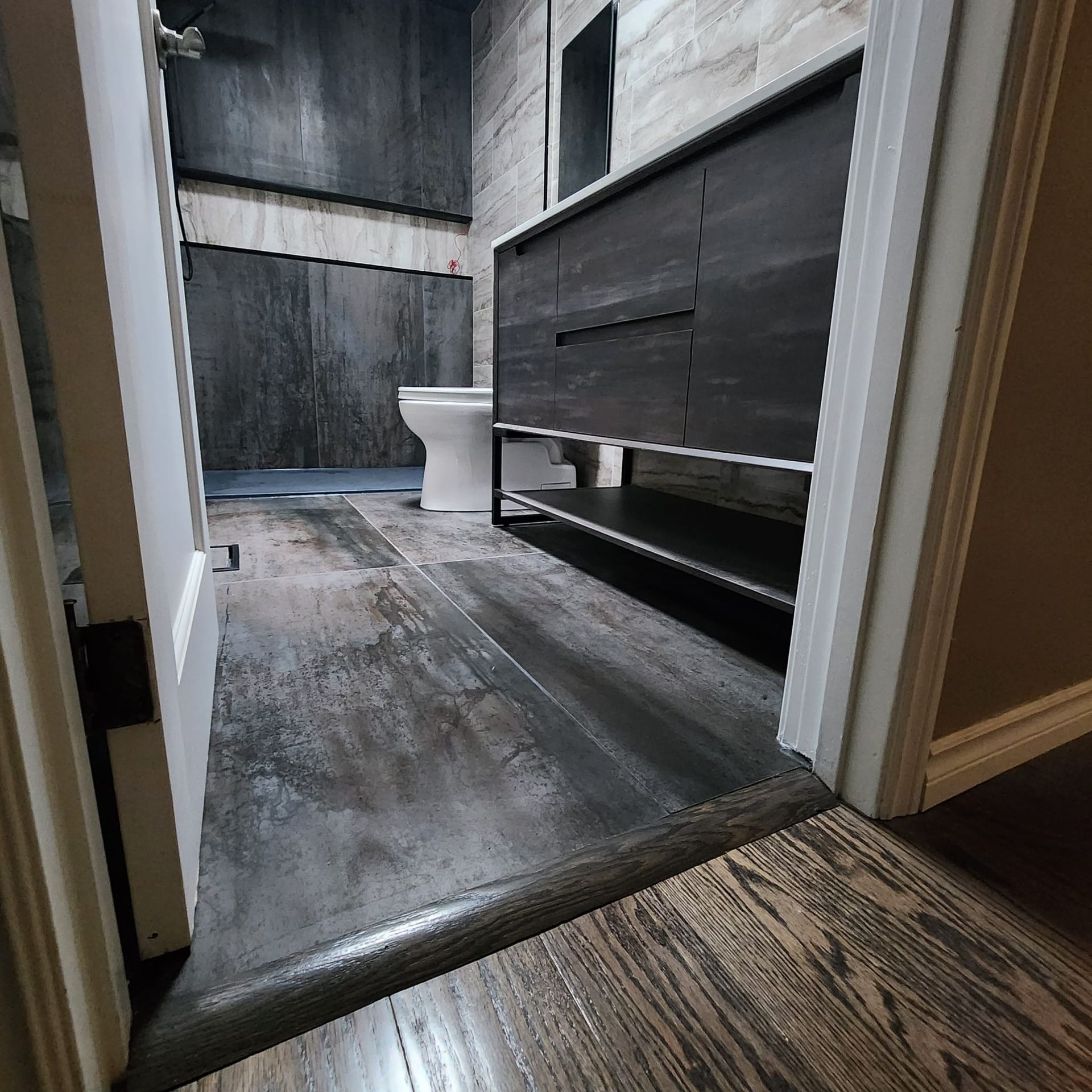 View into a bathroom with dark wood-look flooring and dark vanity. Toilet is visible in the back.