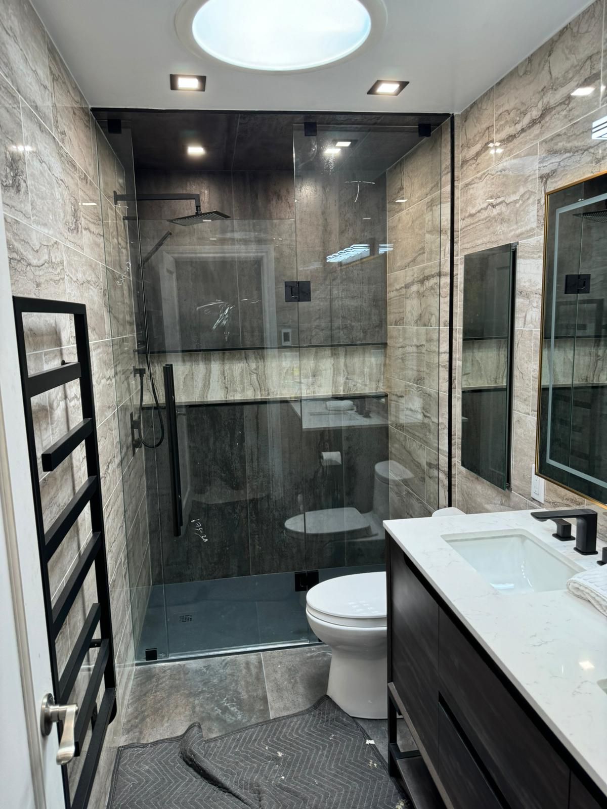Modern bathroom with glass shower, toilet, dark vanity, and heated towel rack.