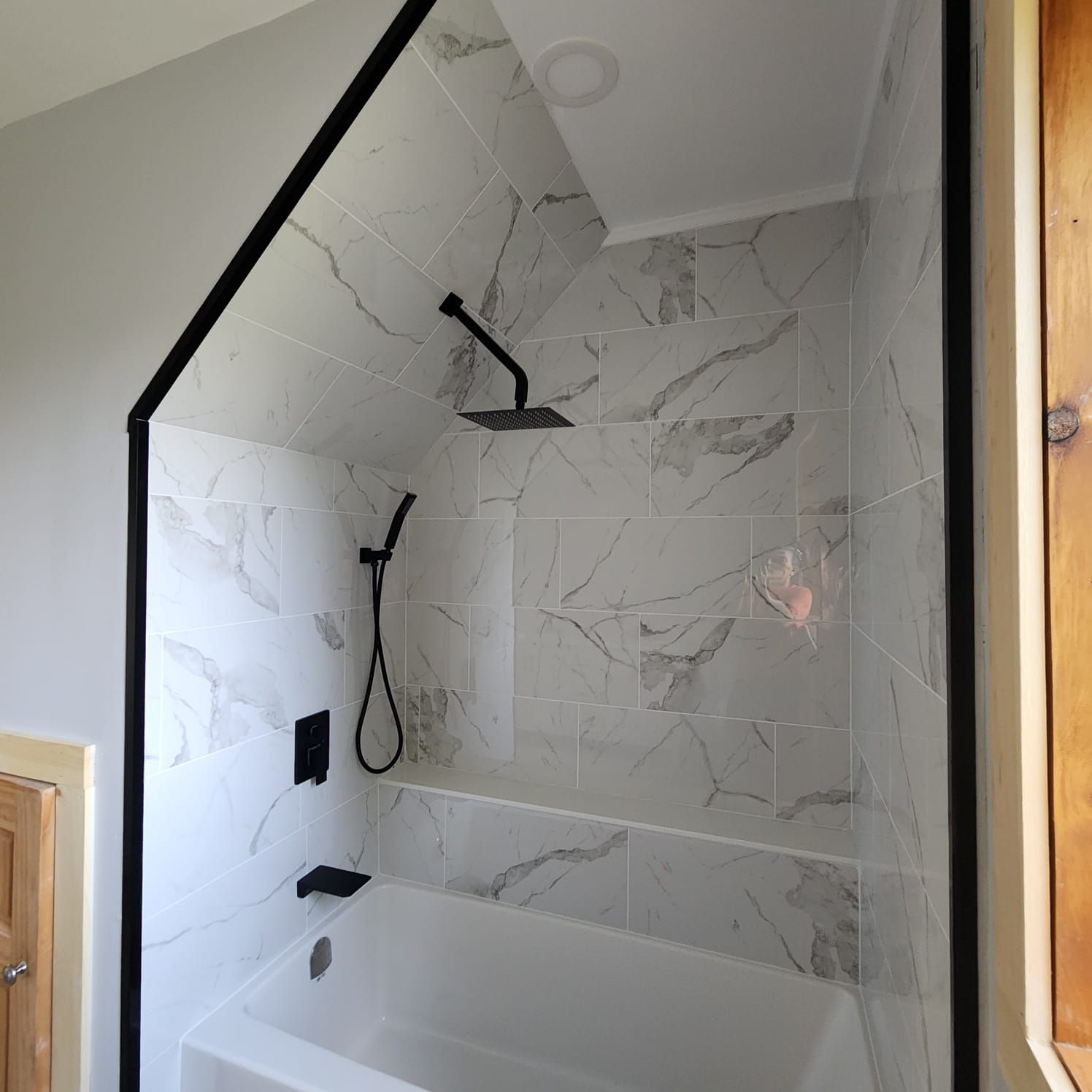 White tiled shower with black trim, fixtures, and a tub.