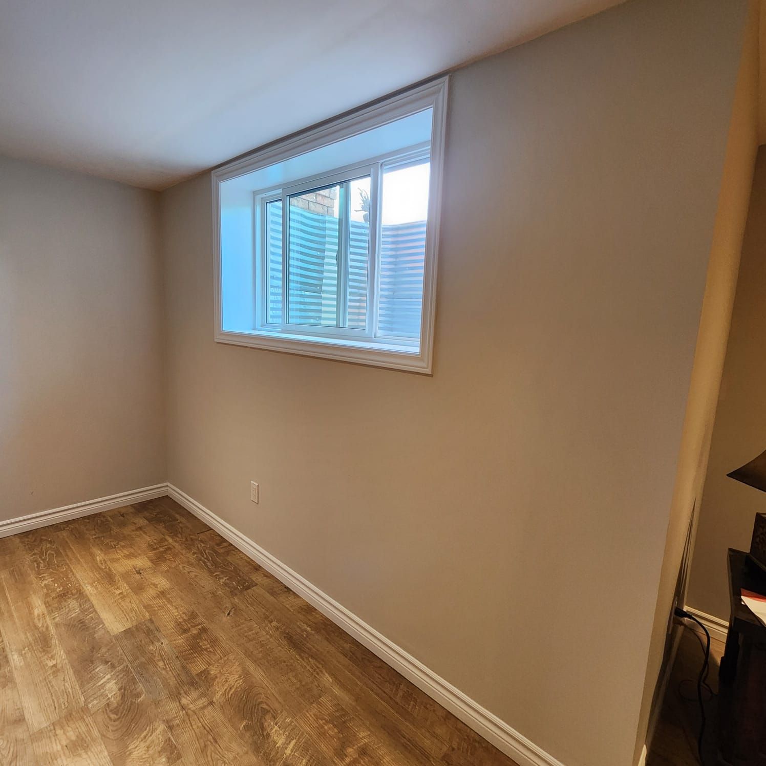 Empty room with wood-look floor, tan walls, and a window with blinds.