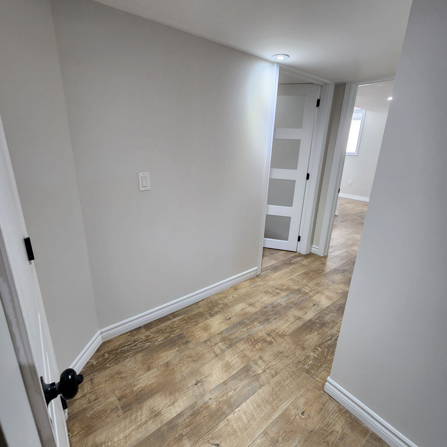 Hallway with wood-look flooring, light gray walls, and white doors. Black doorknob on a closed door.