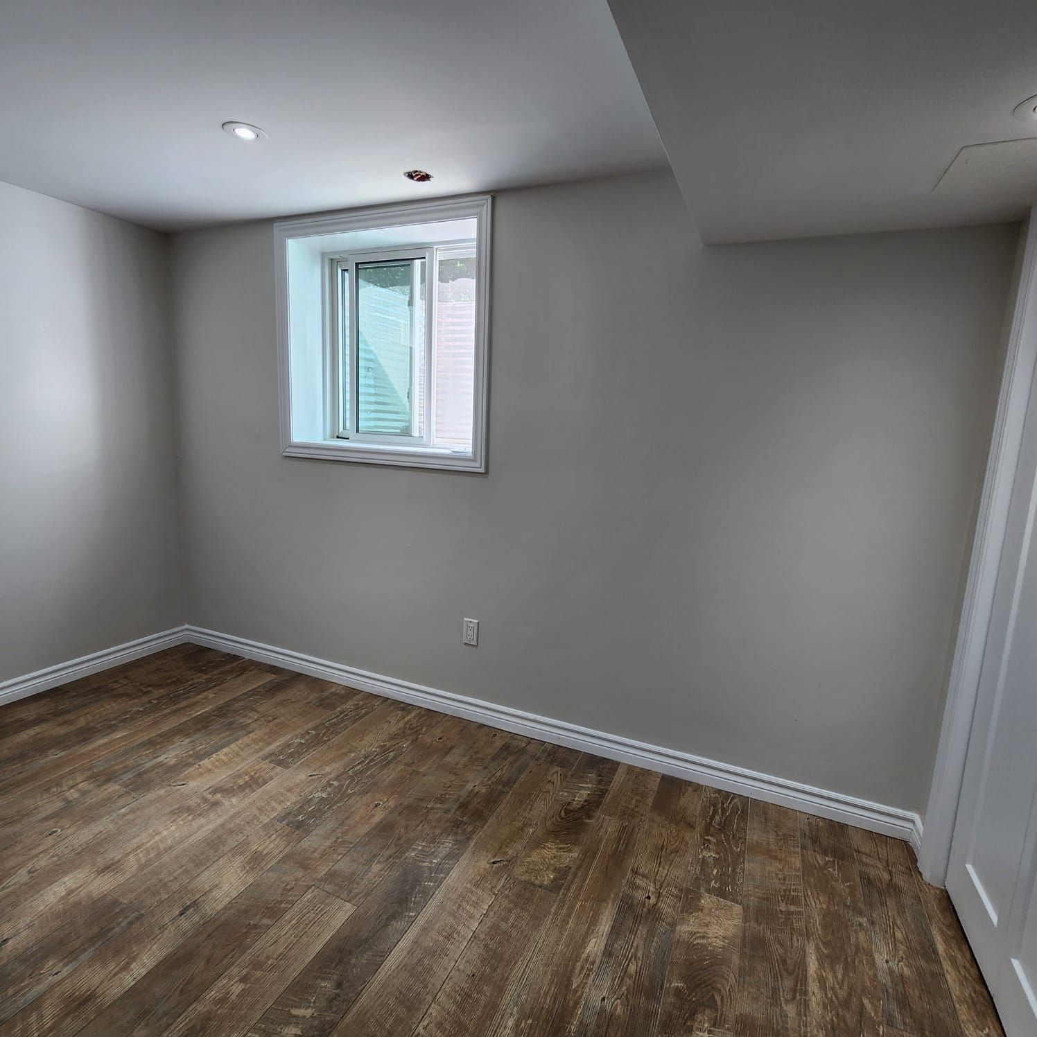 Empty room with wood floors, small window, and grey walls.