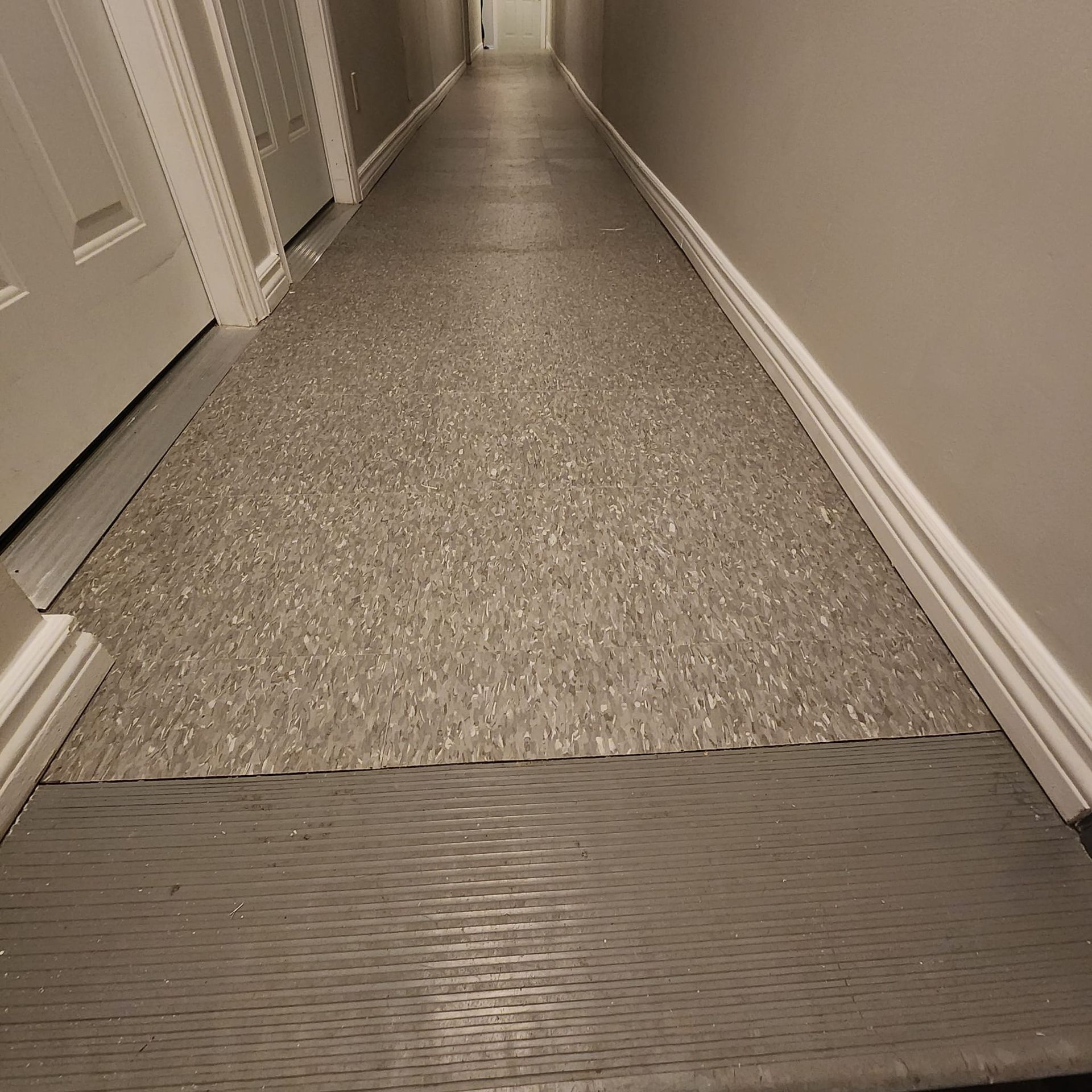 Narrow hallway with gray speckled flooring, white trim, and doors.