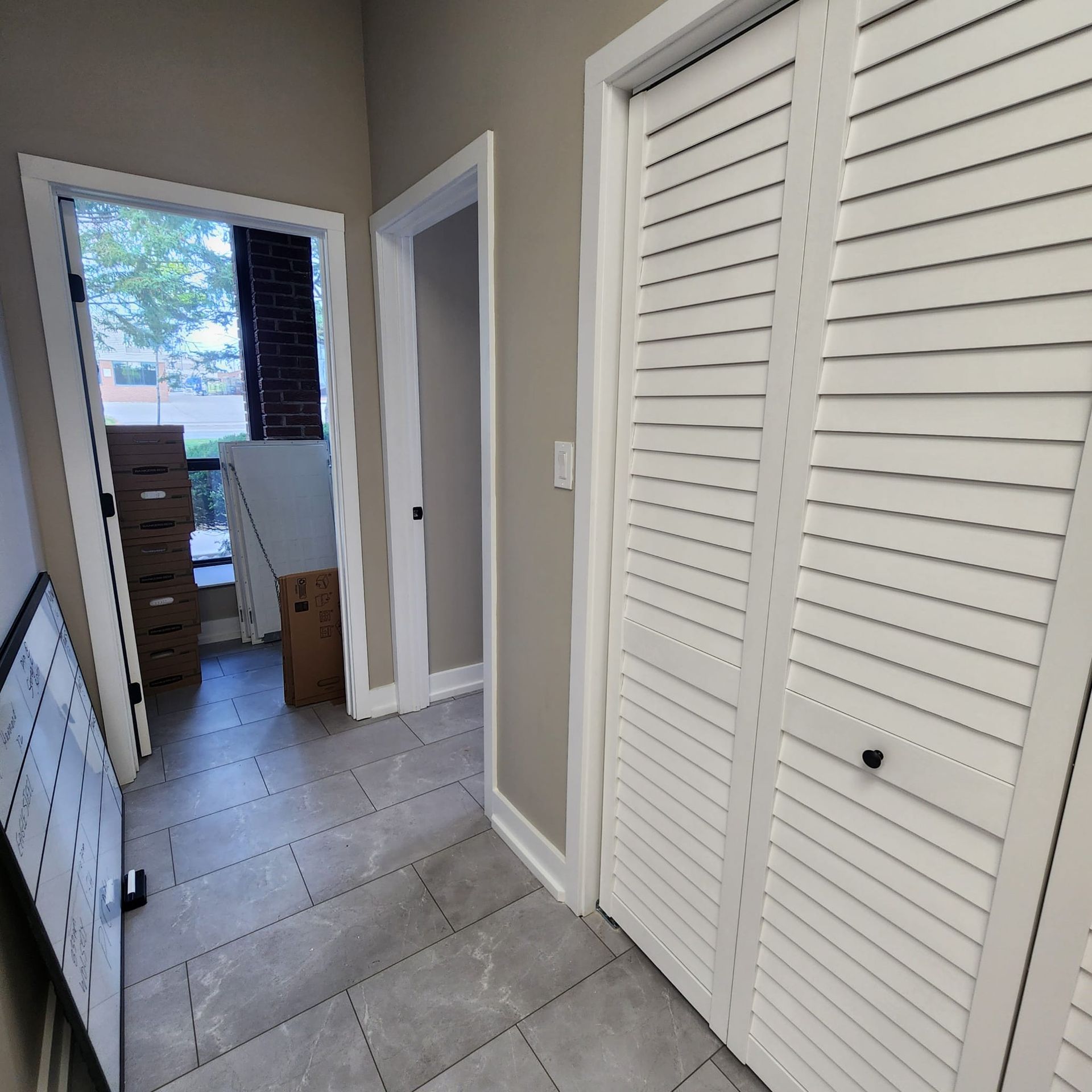 Hallway with tiled floor, white closet doors, and open doorways to a window and another room.